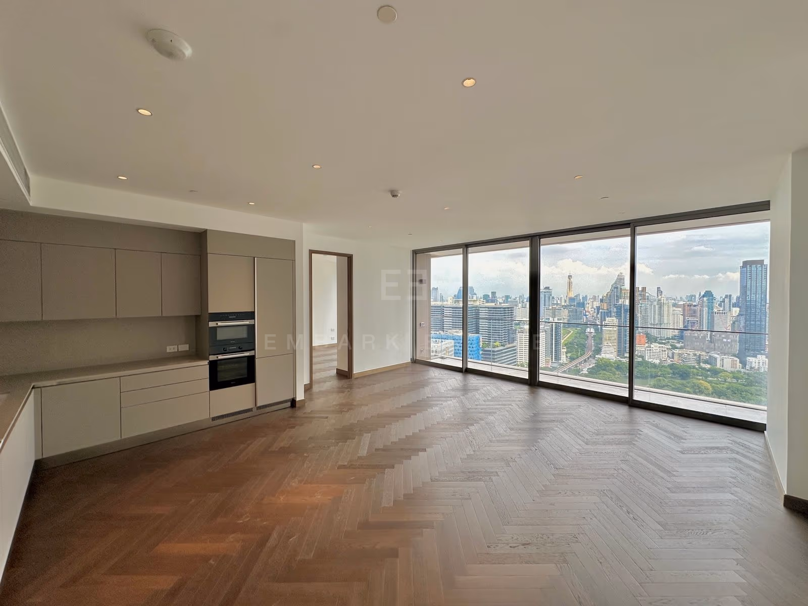 The open living room and kitchen of unit 3202 at Dusit Residences, Dusit Central Park, with floor-to-ceiling glass over Lumphini Park and the city