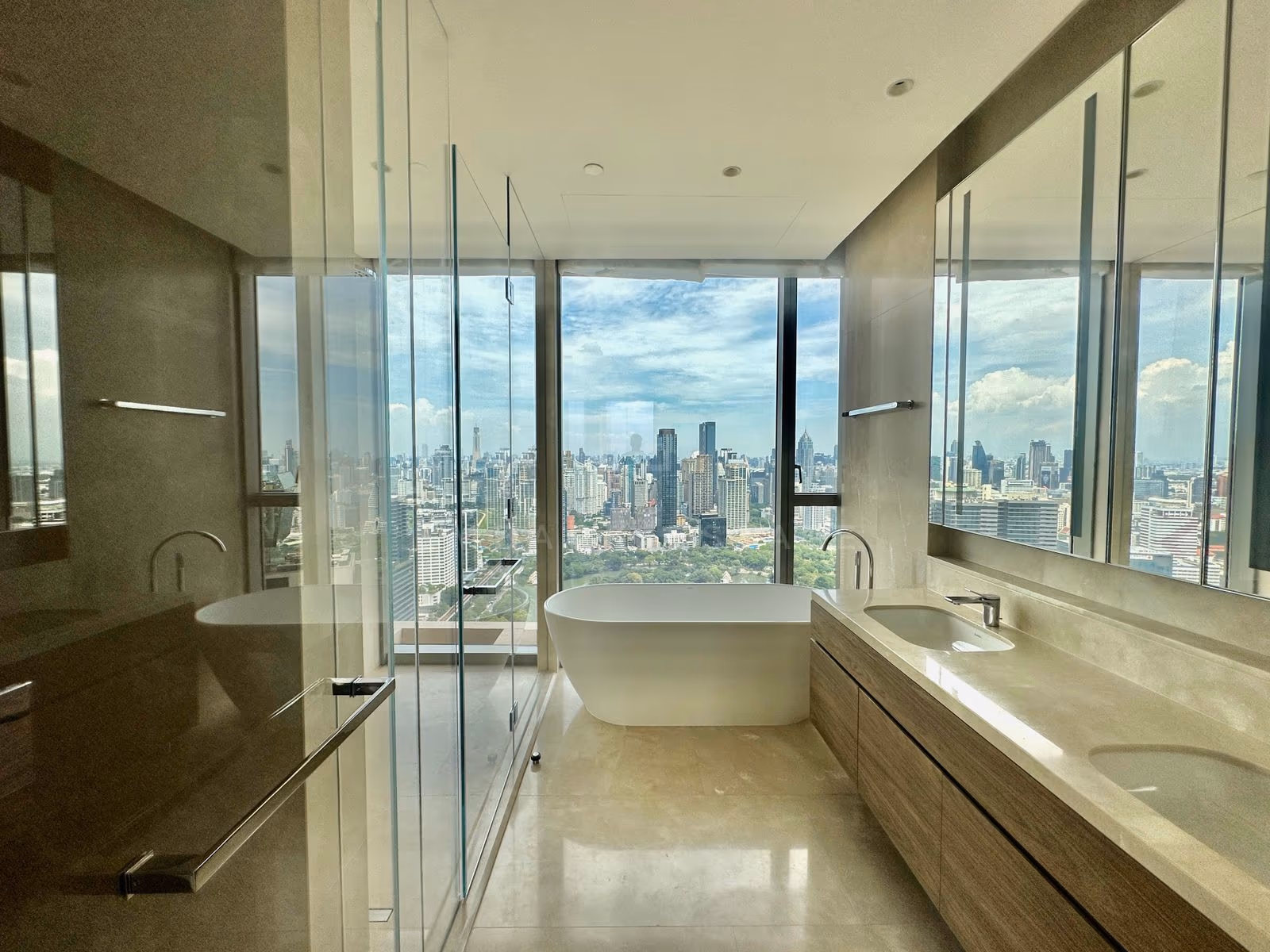 The principal bathroom of unit 3903 at Dusit Residences, Dusit Central Park, a freestanding bathtub set before full-height glass over Lumphini Park, with a glass shower and a double vanity