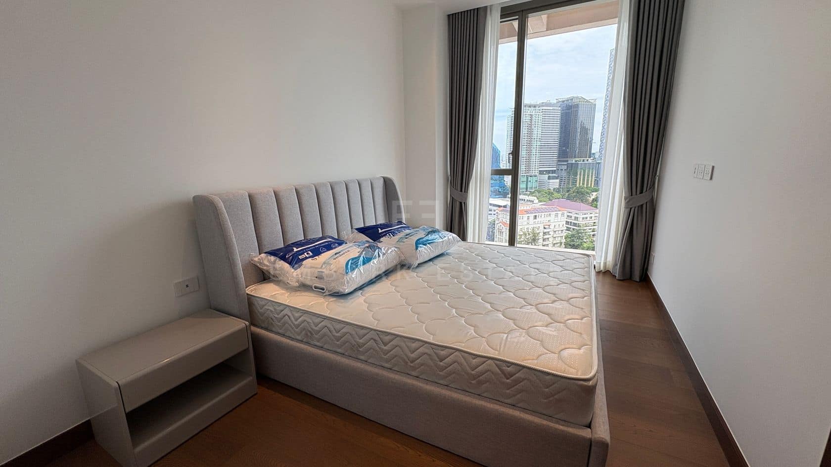 A bedroom of an 86-square-metre two-bedroom residence at Dusit Parkside, Dusit Central Park, Bangkok, with an upholstered bed, a bedside table and a full-height window over the city