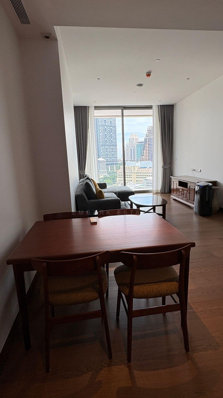 The dining table and living room of an 86-square-metre two-bedroom residence at Dusit Parkside, Dusit Central Park, Bangkok, furnished, with the window and city skyline beyond