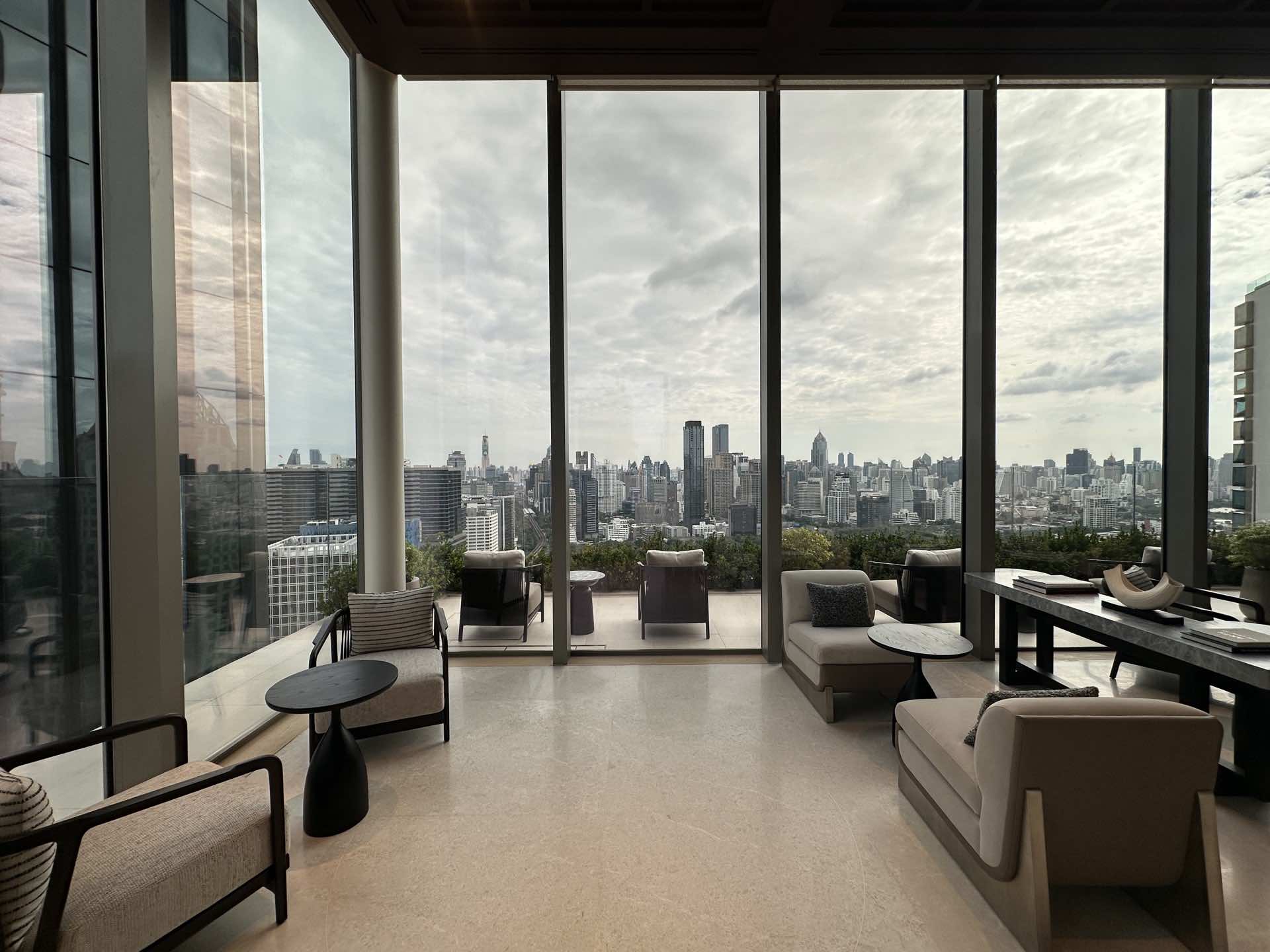 曼谷 Dusit Central Park 的交誼廳:落地玻璃與已佈置的露台懸於樹冠之上,望向曼谷市中心的天際線