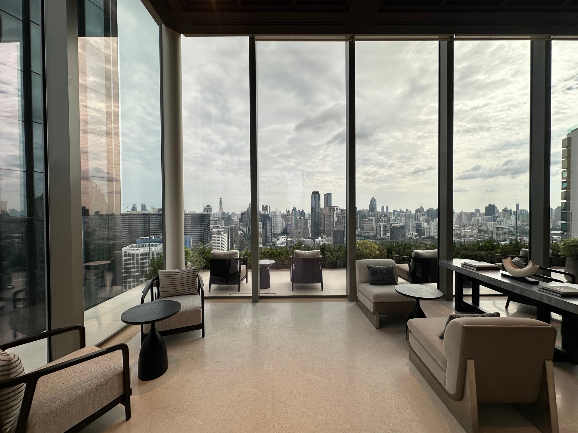 曼谷 Dusit Central Park 的住客會客廳:落地玻璃與已佈置的露台懸於樹冠之上,望向曼谷市中心的天際線