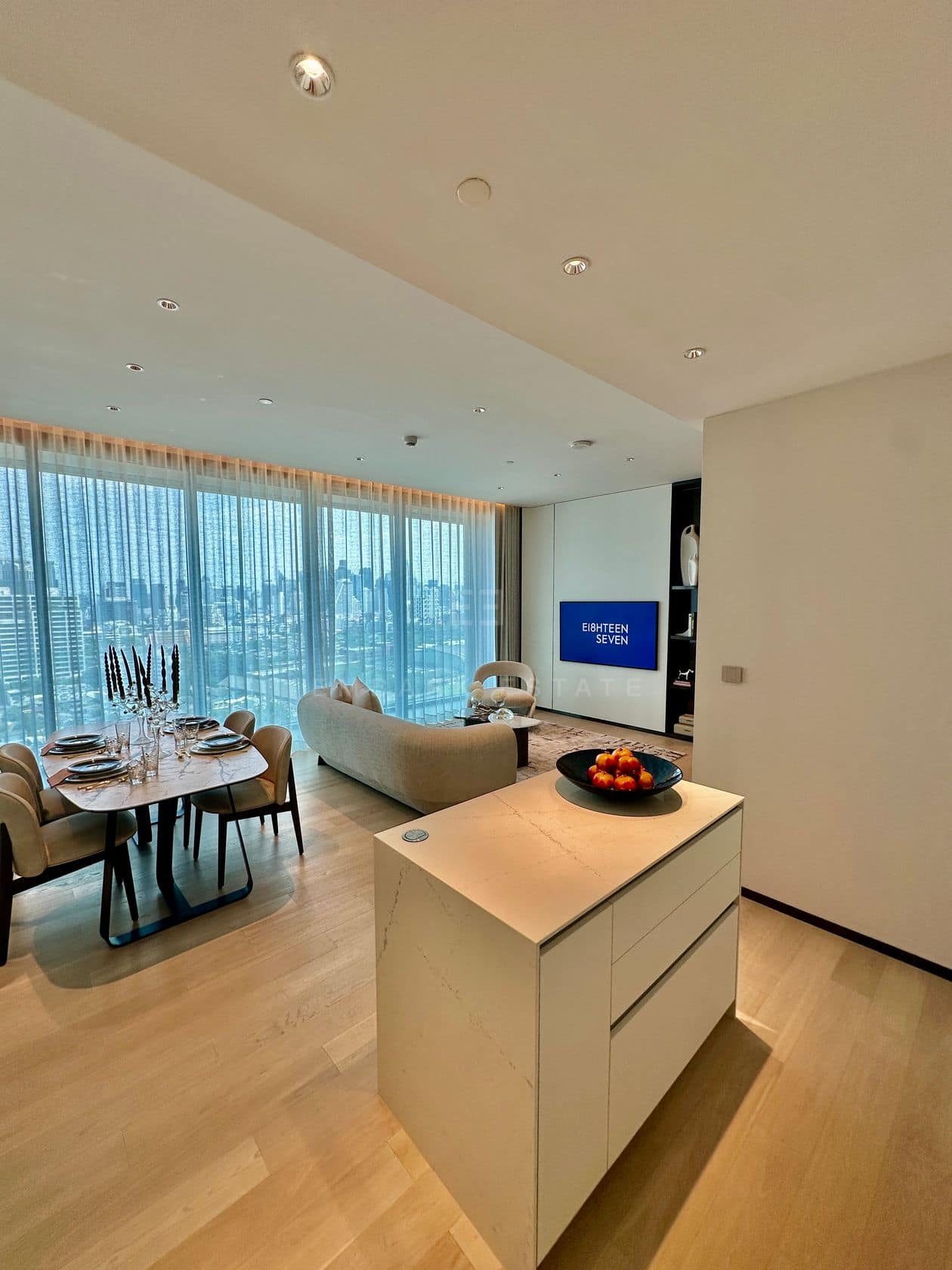 The open-plan living, dining and kitchen of a two-bedroom residence at EI8HTEEN SEVEN, One Bangkok, with a marble island and floor-to-ceiling windows