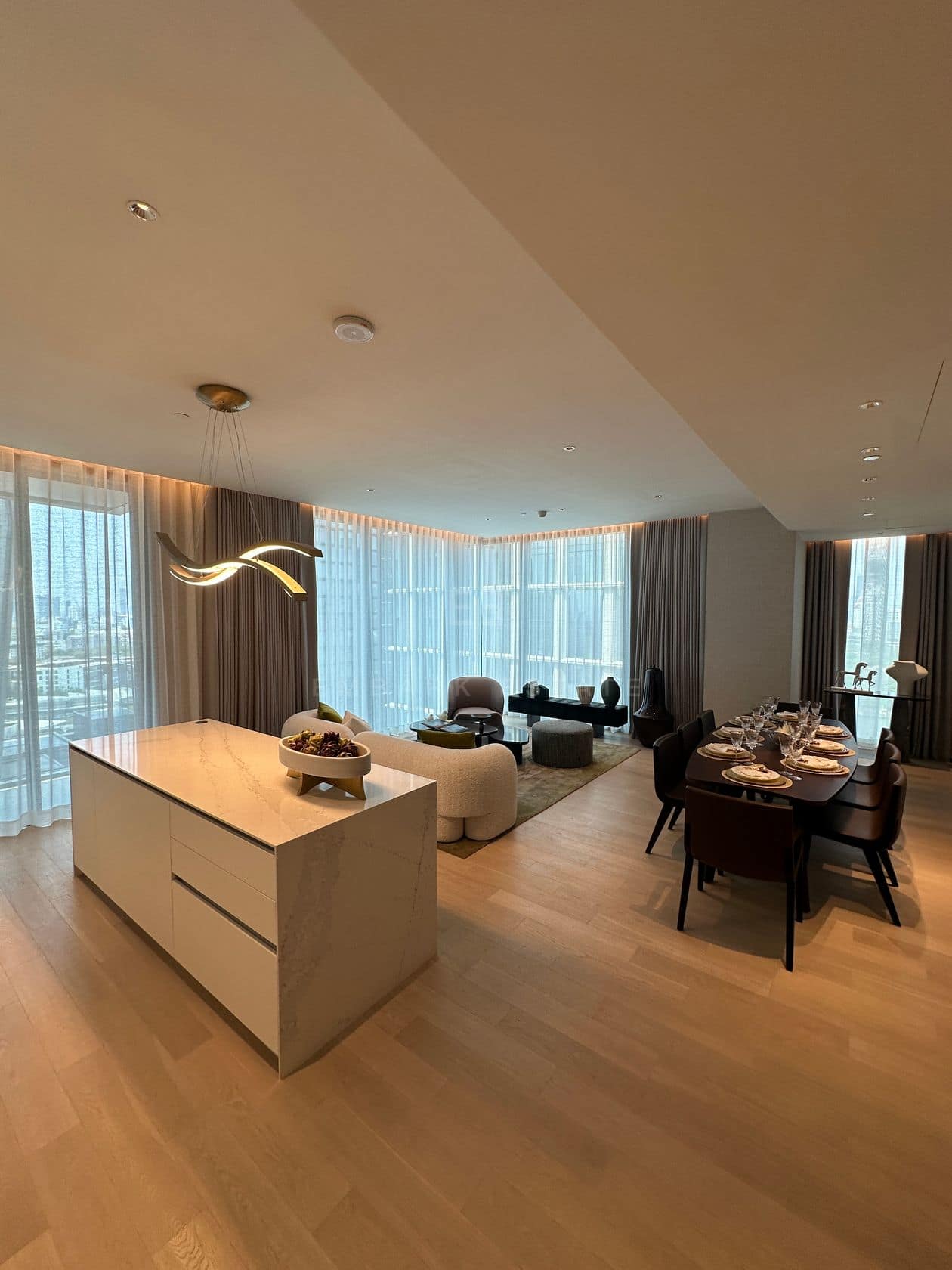 The living room of a three-bedroom residence at EI8HTEEN SEVEN, One Bangkok, with a marble island, curved sofa and dining table in one open-plan space