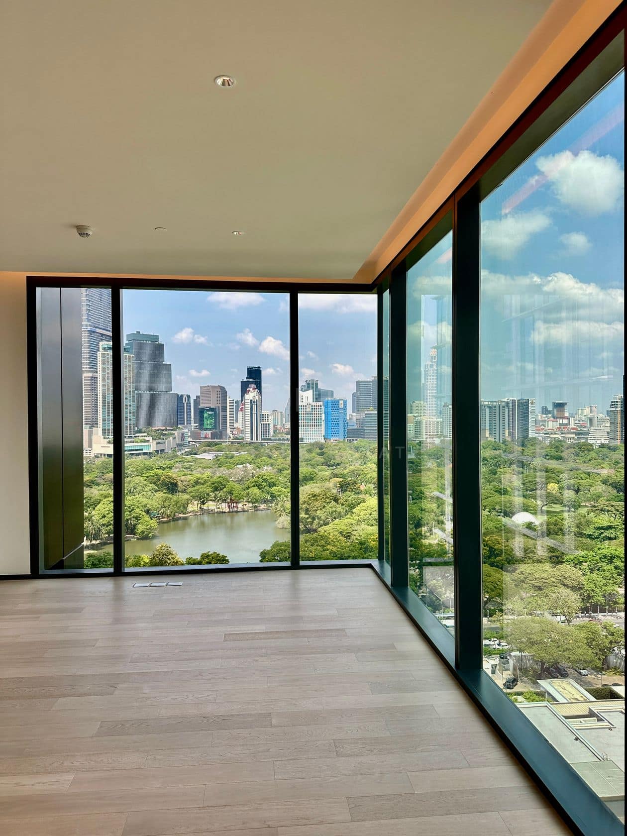 A corner room of an unfurnished three-bedroom residence at EI8HTEEN SEVEN, One Bangkok, with floor-to-ceiling glass over the Lumphini Park lake and the city