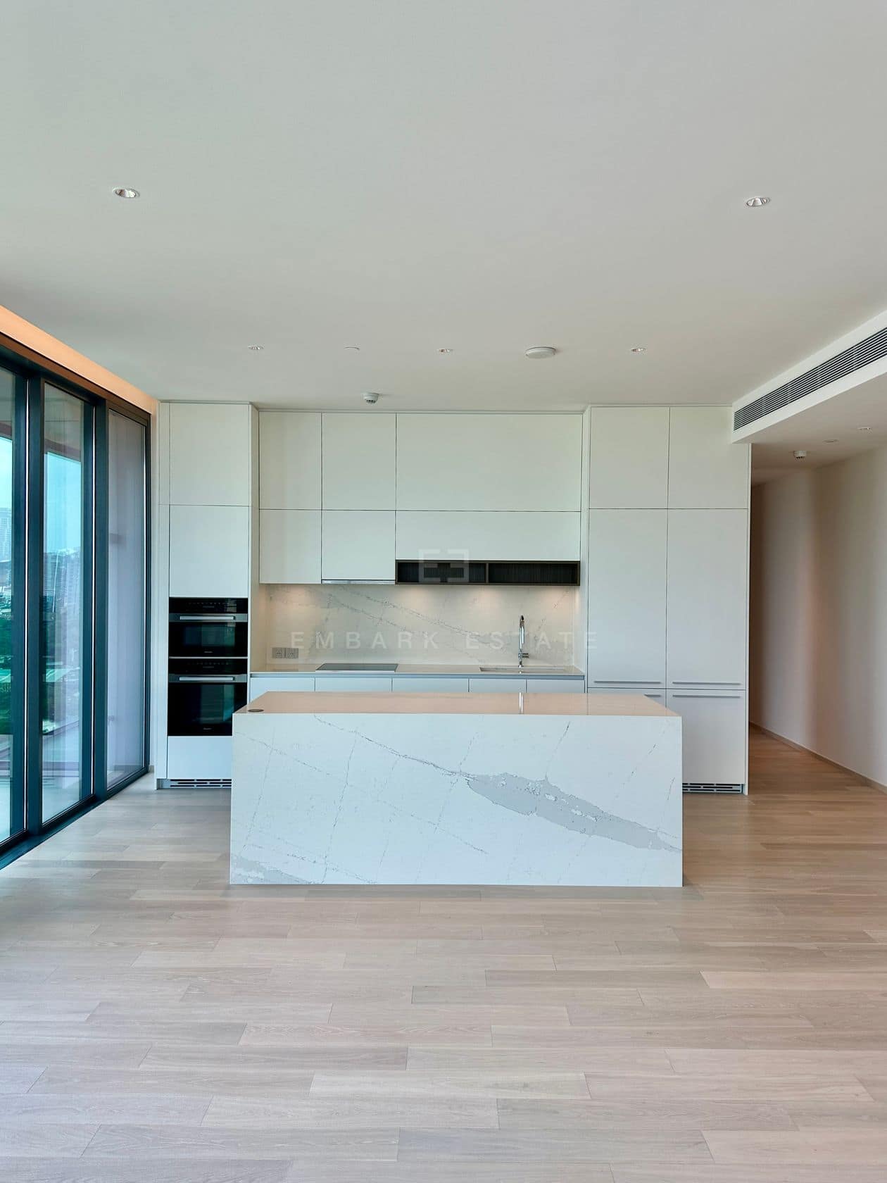 The kitchen of an unfurnished three-bedroom residence at EI8HTEEN SEVEN, One Bangkok, with a marble waterfall island, integrated wine fridges and Miele appliances