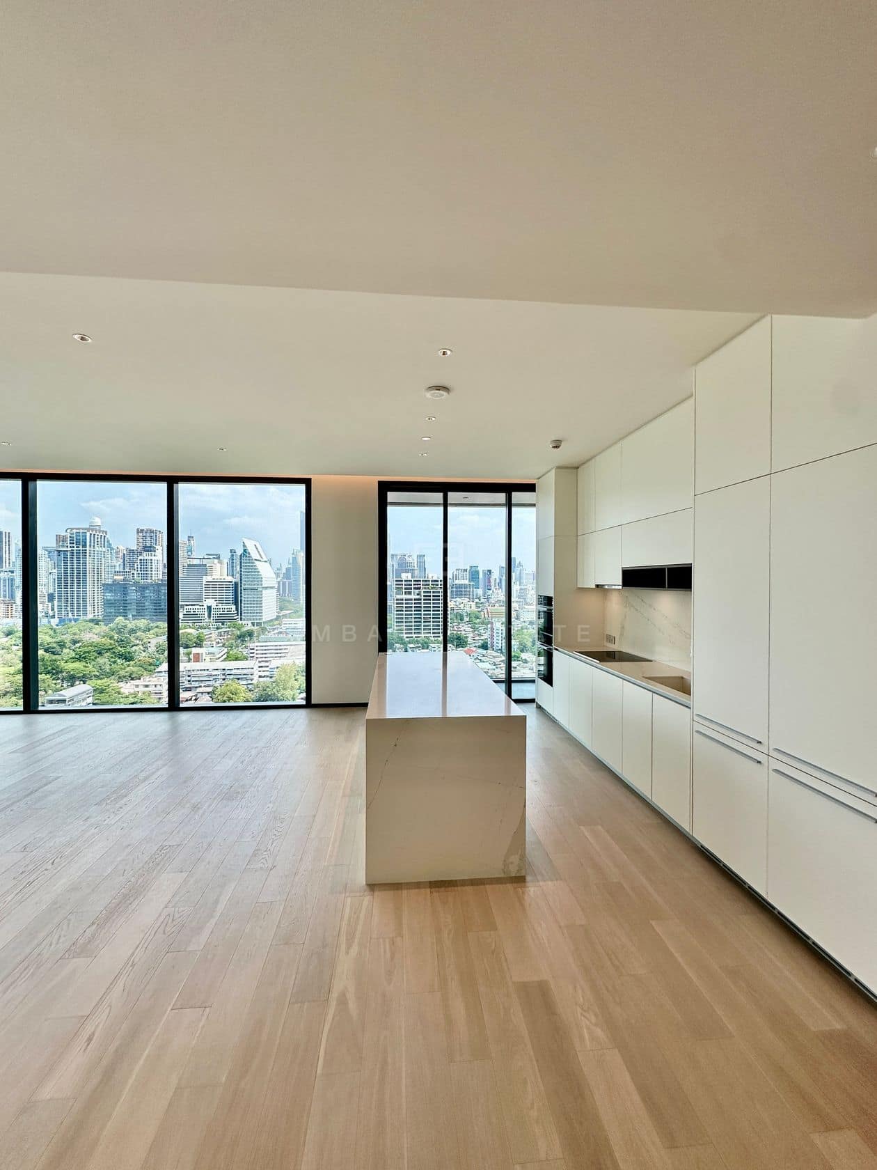 The open-plan living and kitchen of an unfurnished three-bedroom residence at EI8HTEEN SEVEN, One Bangkok, with a marble island and floor-to-ceiling views over Lumphini Park and the central Bangkok skyline
