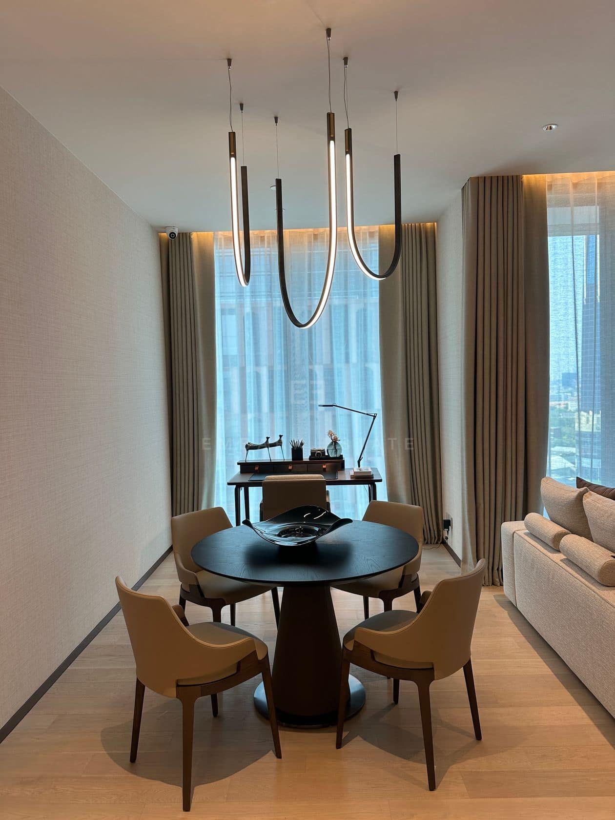 The dining table of a one-bedroom residence at EI8HTEEN SEVEN, One Bangkok, beneath sculptural pendants with a city view