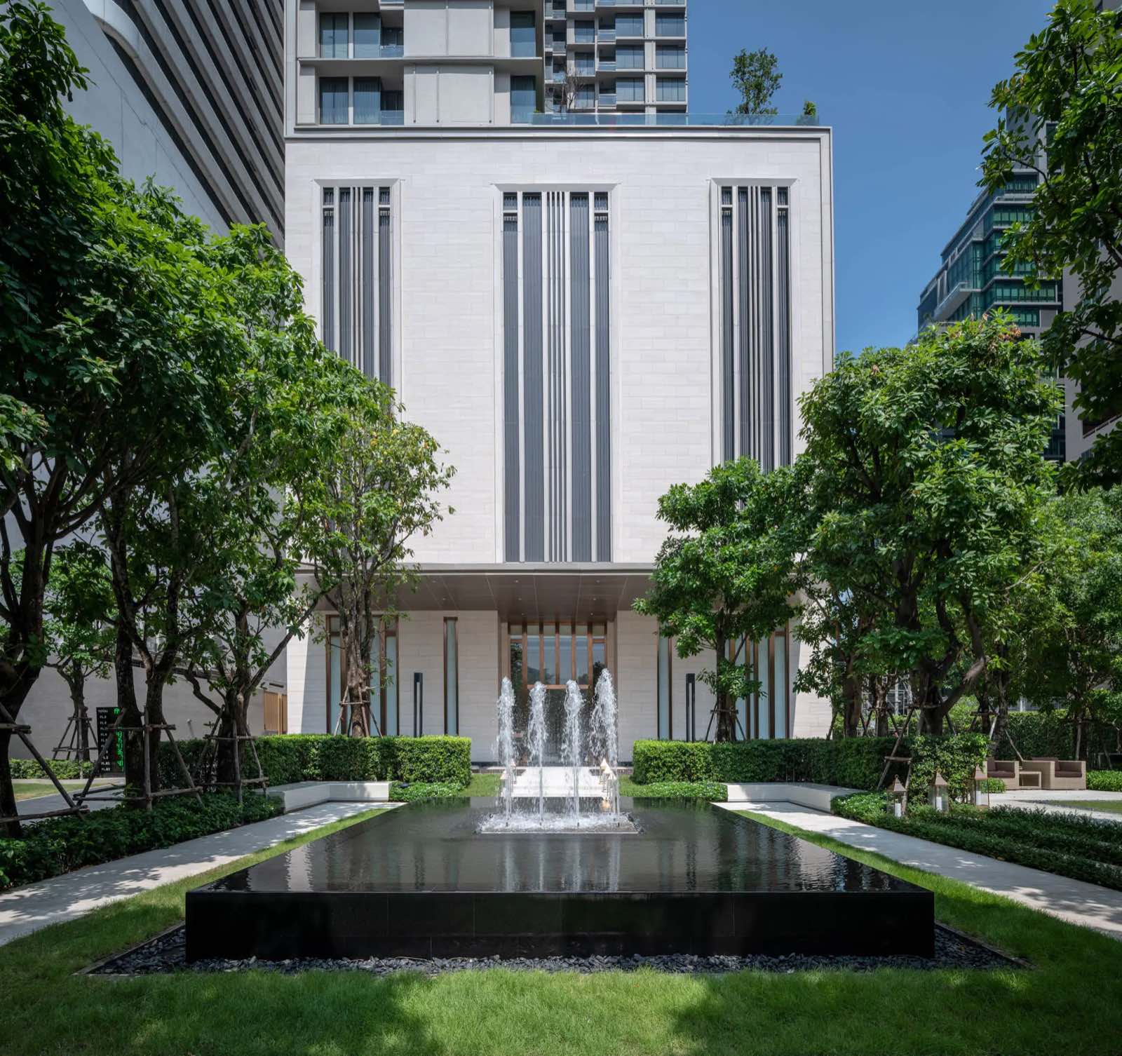 The ESSE Asoke: Daytime arrival garden with a central fountain pool and the stone facade of The ESSE Asoke behind