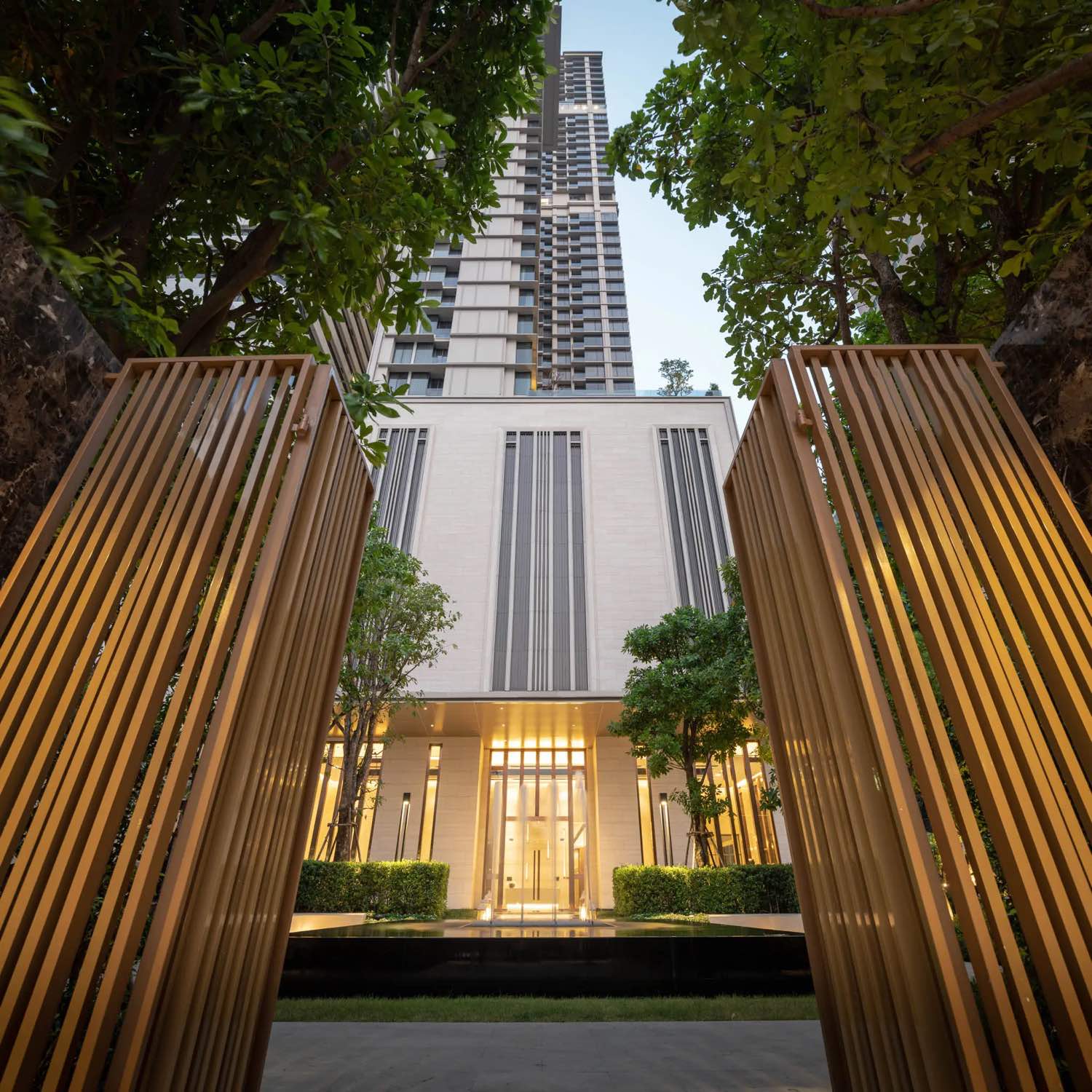 The ESSE Asoke: The ESSE Asoke tower rising through the golden vertical-fin gateway above the entrance court at dusk