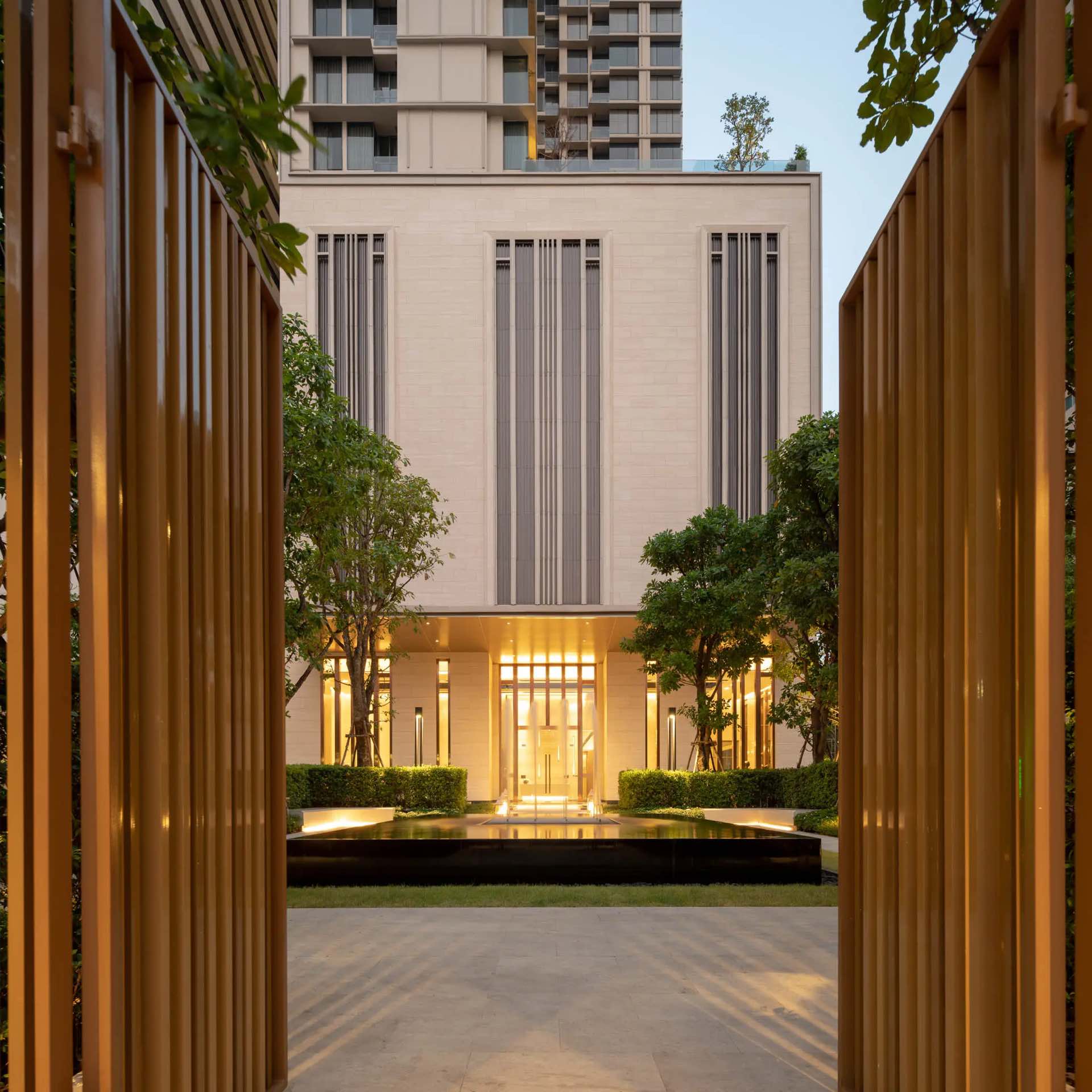 The ESSE Asoke: Full-height view of The ESSE Asoke tower and stone-clad base entrance seen between the brass gateway fins