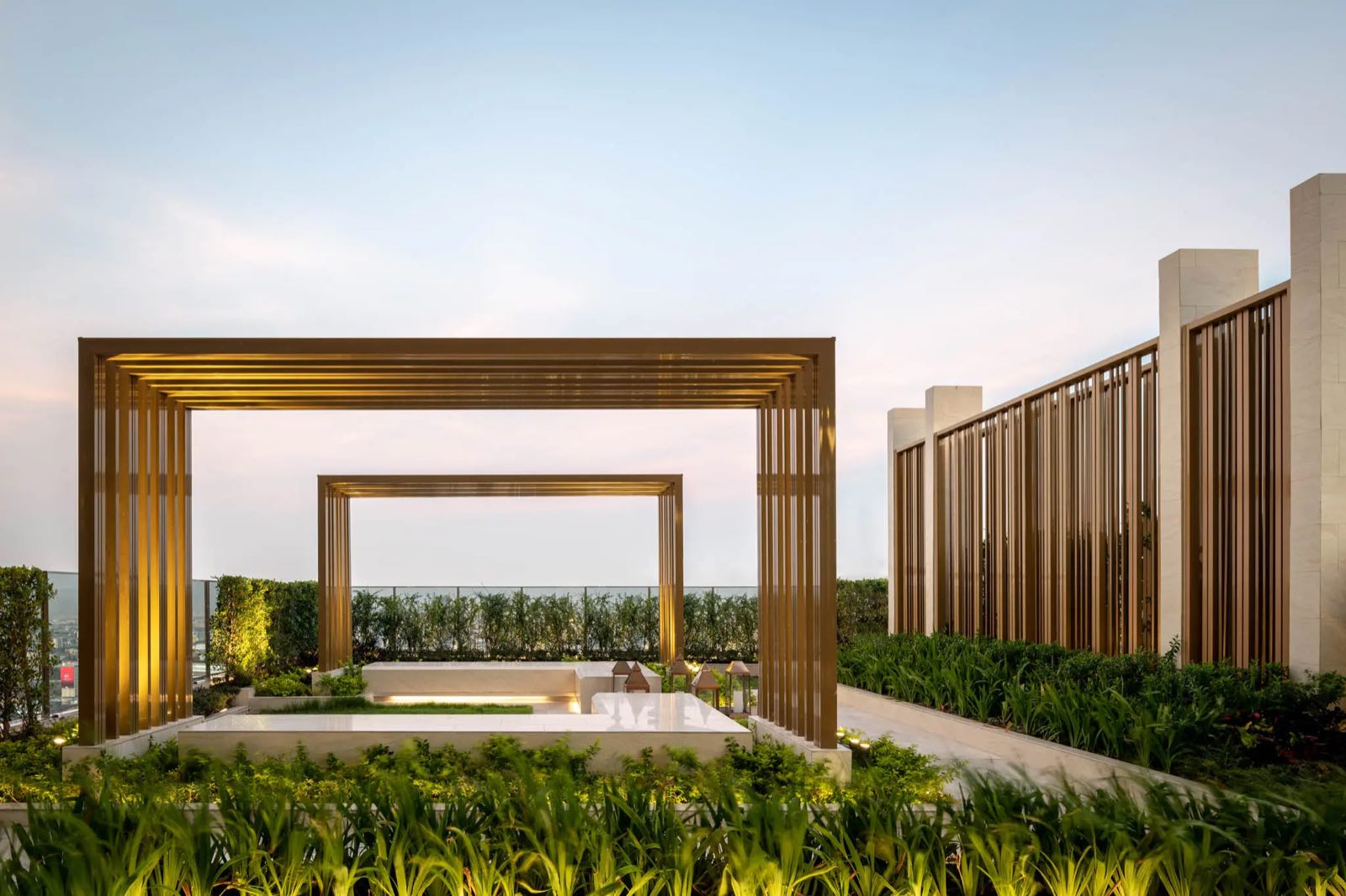 The ESSE Asoke: Rooftop garden pavilion with brass pergolas and a sunken lounge among planting at twilight