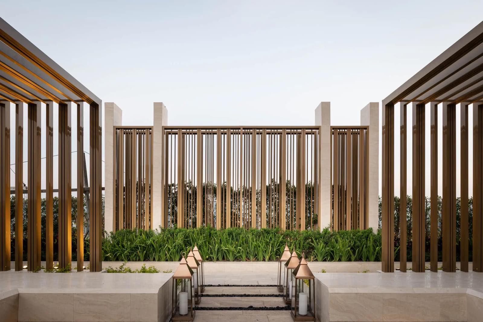 The ESSE Asoke: Rooftop sky garden terrace with brass vertical screens framing the city beyond at dusk