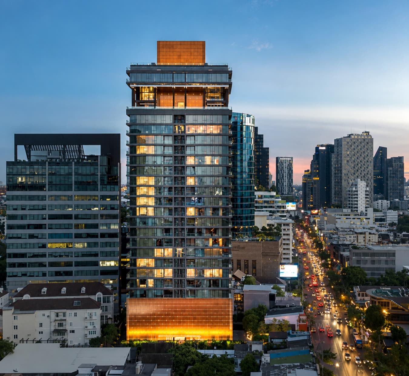 KHUN by YOO: the tower lit gold at dusk with its illuminated lobby, above the Thonglor skyline in central Bangkok, by Sansiri and YOO