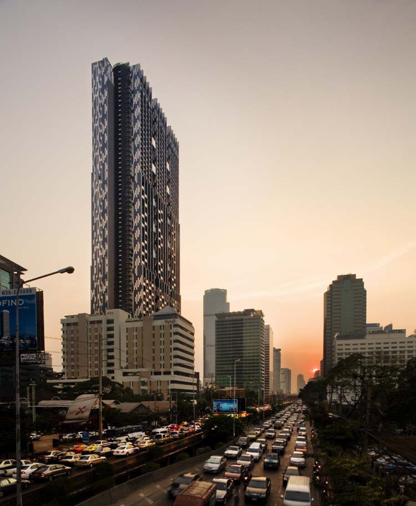 The Met Sathorn: The Met tower on Sathorn Road at sunset, its dark facade rising above the street and traffic