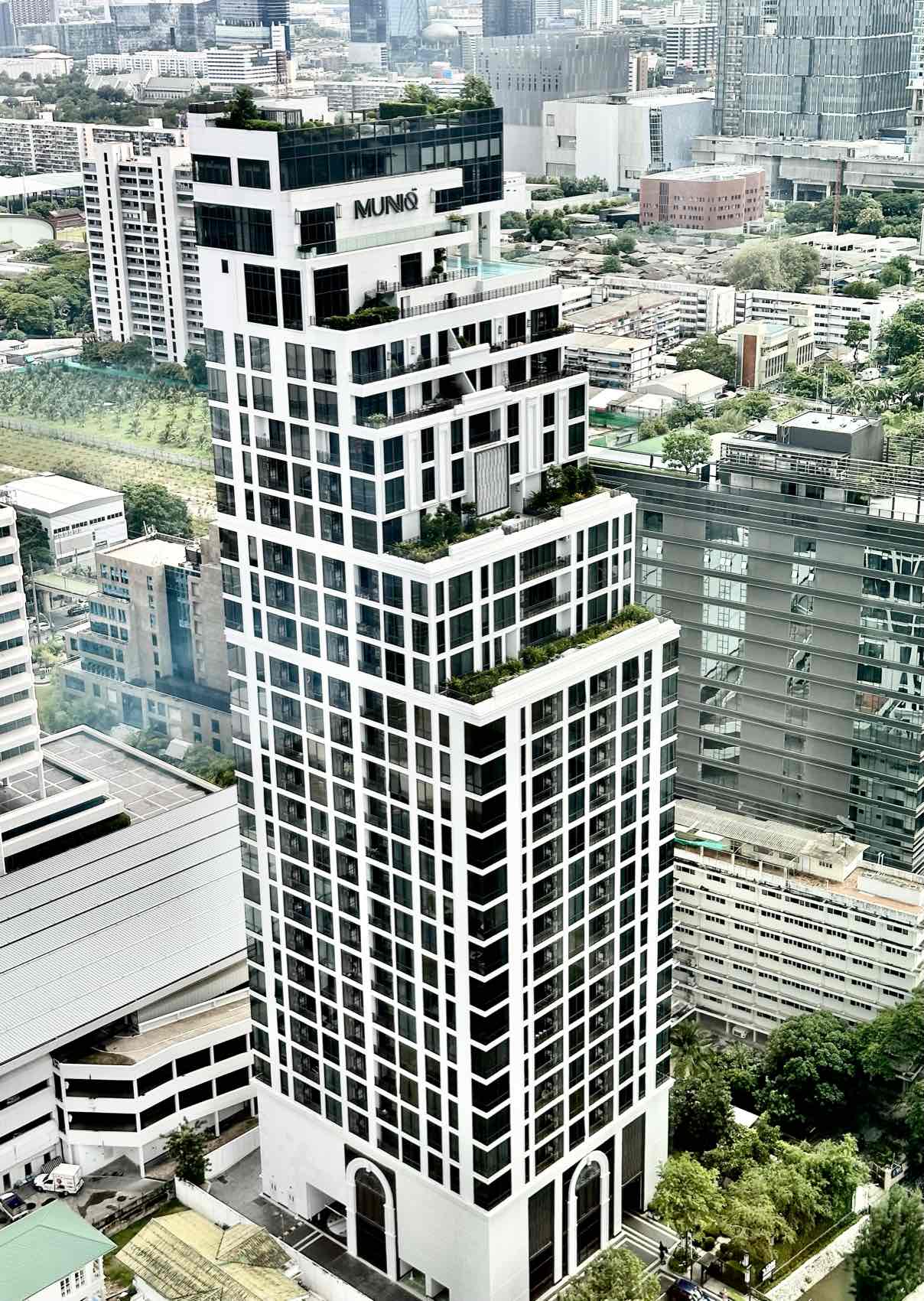MUNIQ Langsuan: the tower and its rooftop pool seen from street level with the MUNIQ signage