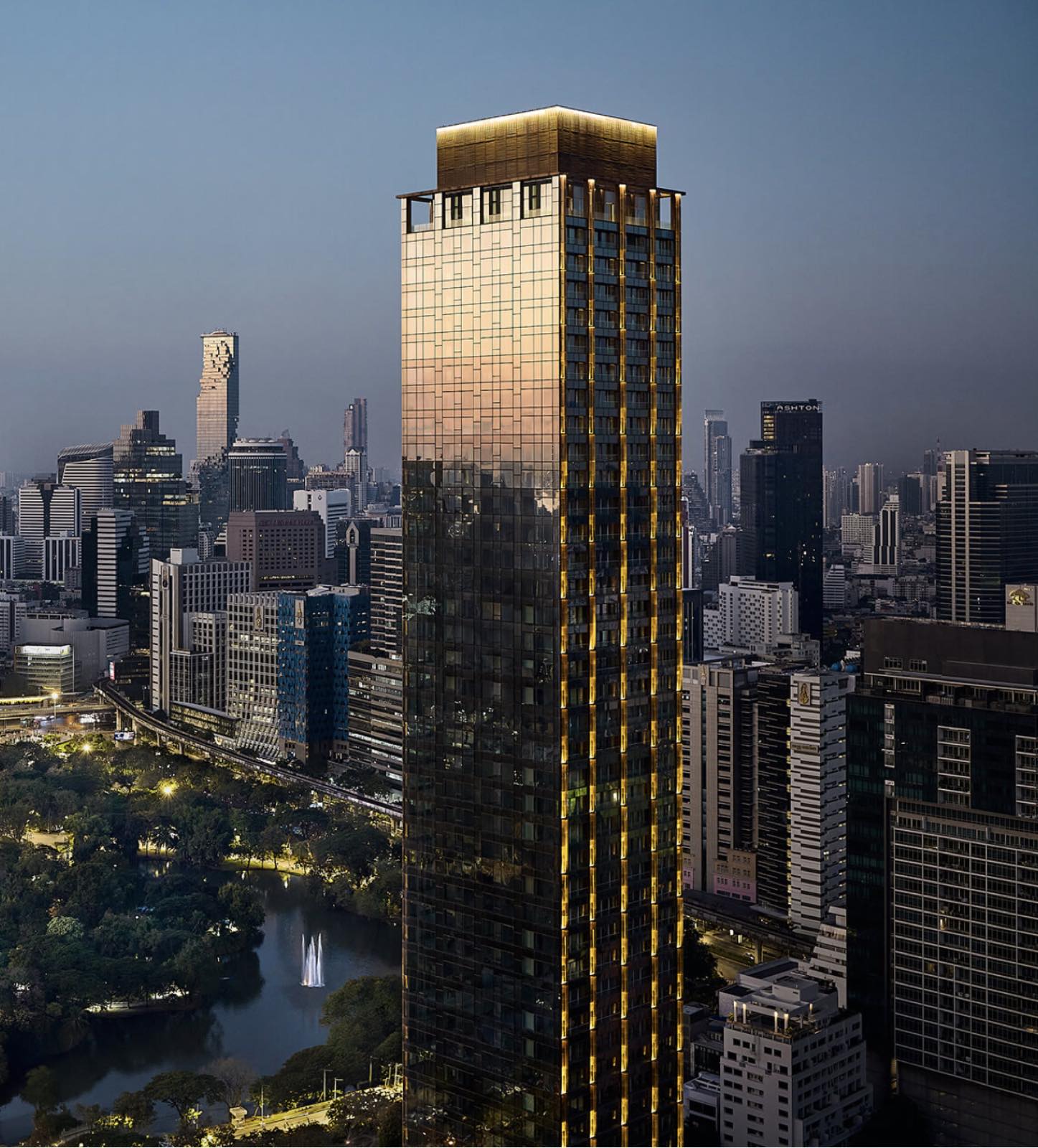 NIMIT Lumphini Park North tower at dusk over Lumphini Park, golden facade lit against the Bangkok skyline