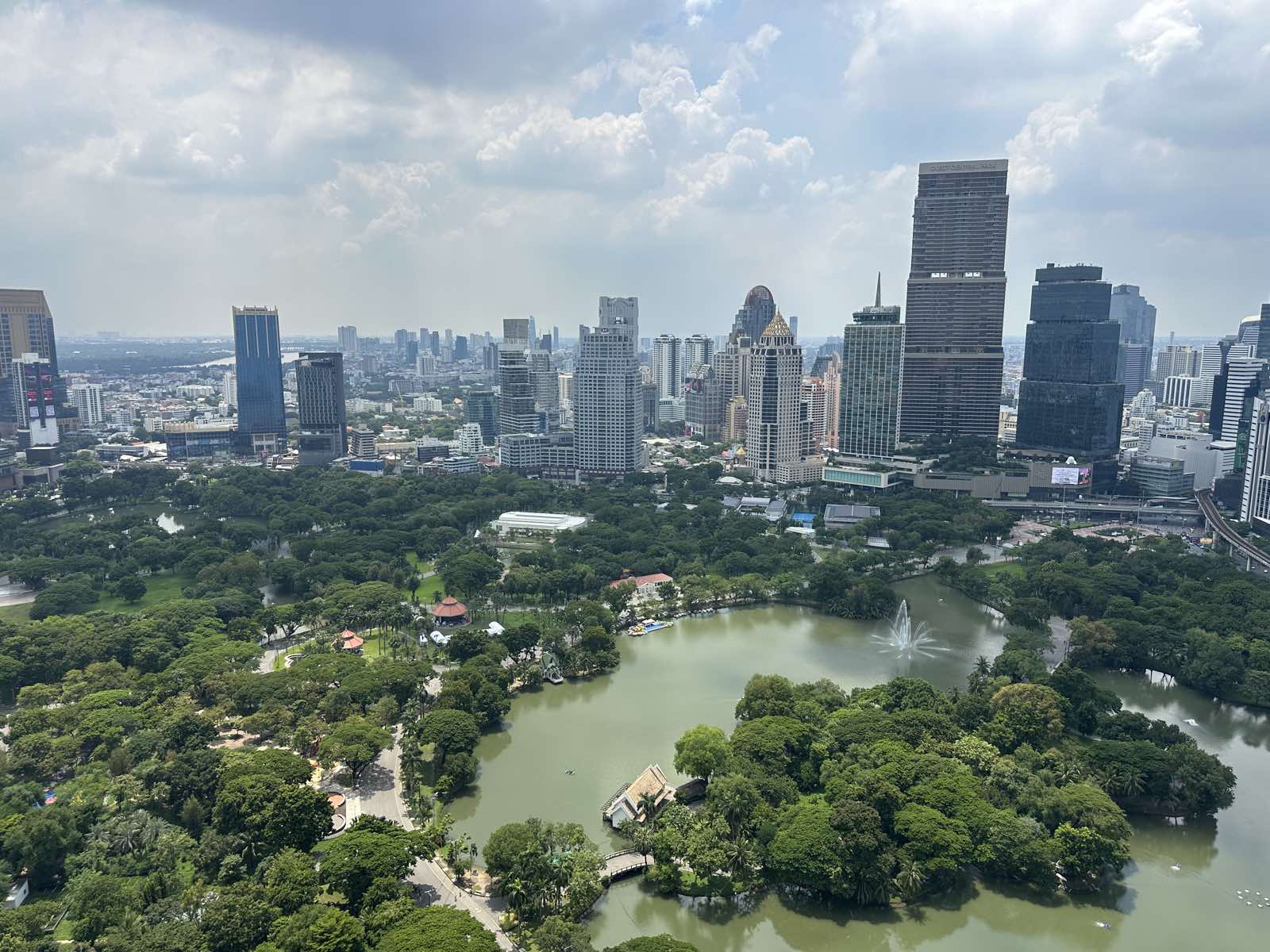 The view south from a residence at NIMIT Lumphini Park North in Bangkok: the whole of Lumphini Park with its lake and fountain, Dusit Central Park and the Sathorn skyline beyond, photographed October 2026