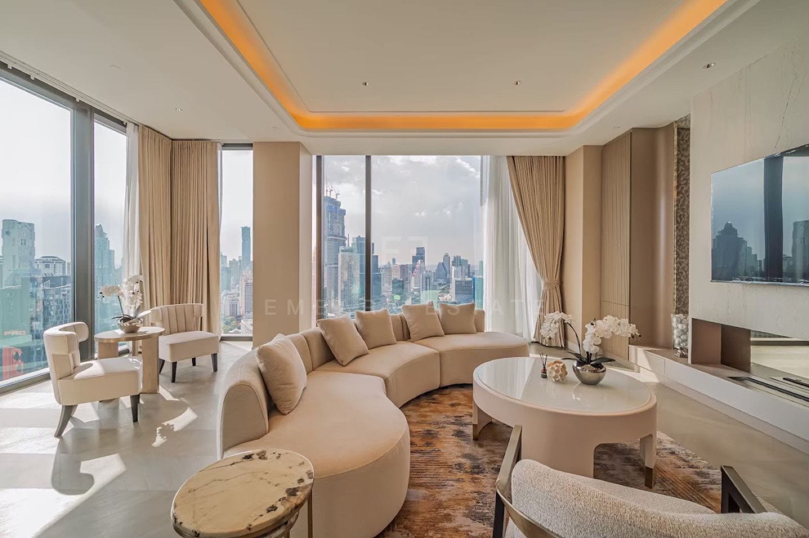 The living room of a three-bedroom residence at ONE89 Wireless, One Bangkok, with a curved sofa beneath a soft cove-lit ceiling, facing the central Bangkok skyline