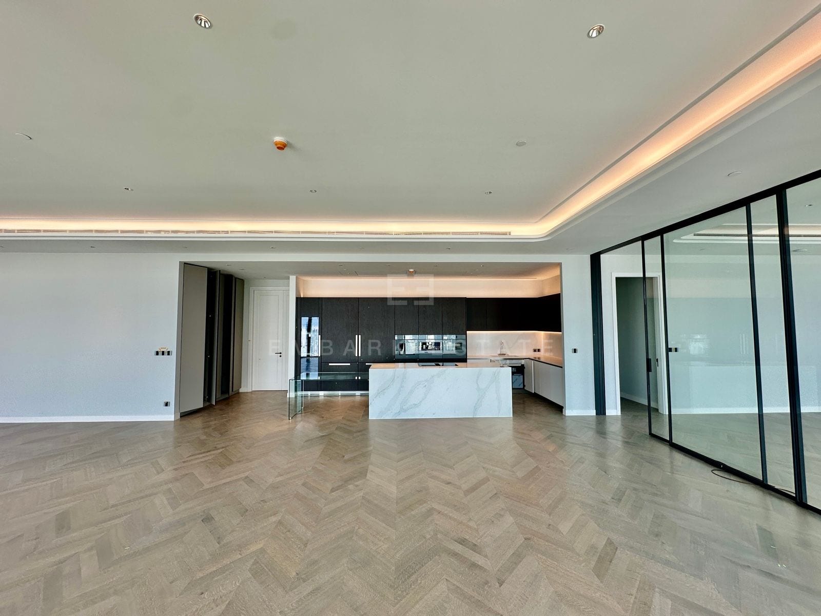 The open-plan kitchen and living area of the 5-bedroom grand penthouse at ONE89 Wireless, One Bangkok, with a marble island and dark timber joinery