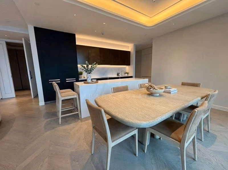 Kitchen and dining area of a two-bedroom residence at ONE89 Wireless, with tall black cabinetry, a white stone island with bar seating and a whitewashed oak dining table with upholstered chairs.