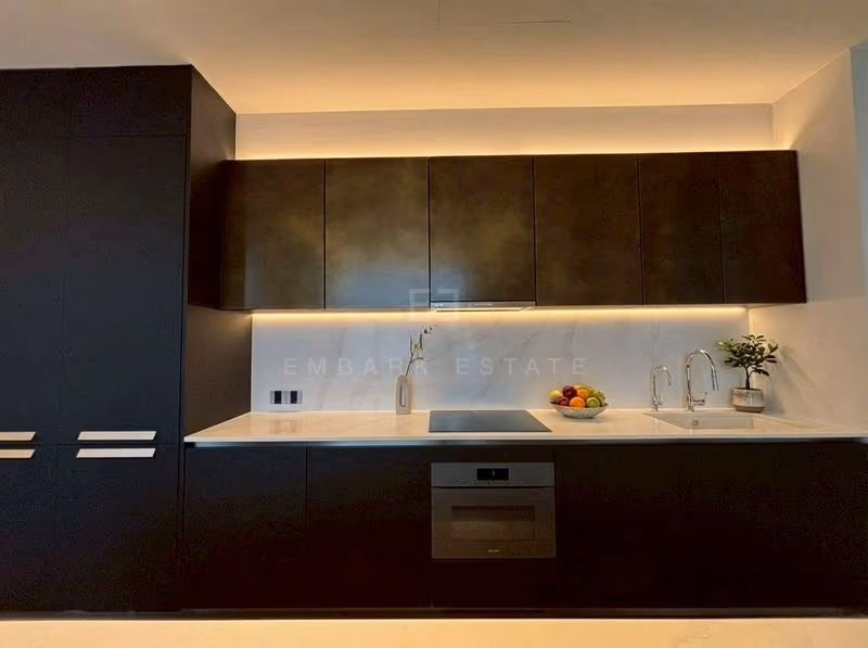 Kitchen of a two-bedroom residence at ONE89 Wireless, with dark bronze wall cabinets lit from below, a white stone backsplash, an induction hob, a built-in oven and a sink with two taps.