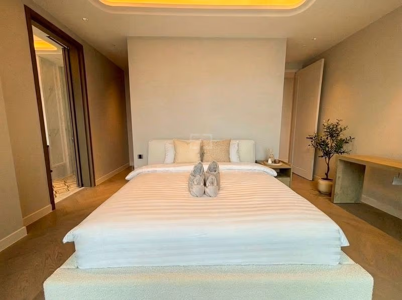 Principal bedroom of a two-bedroom residence at ONE89 Wireless, with a cream upholstered bed under a cove-lit ceiling and an open doorway to a marble en-suite bathroom.