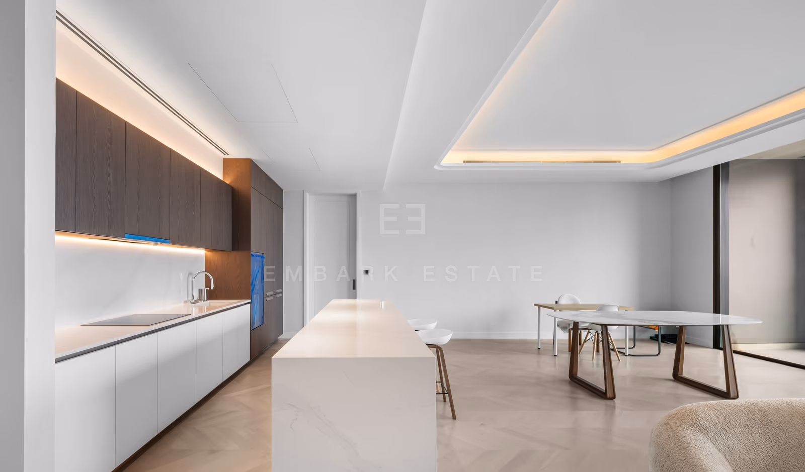 Kitchen of a three-bedroom residence at ONE89 Wireless, Bangkok, with a white stone island, a run of dark timber cabinets and the dining table and living room beyond.
