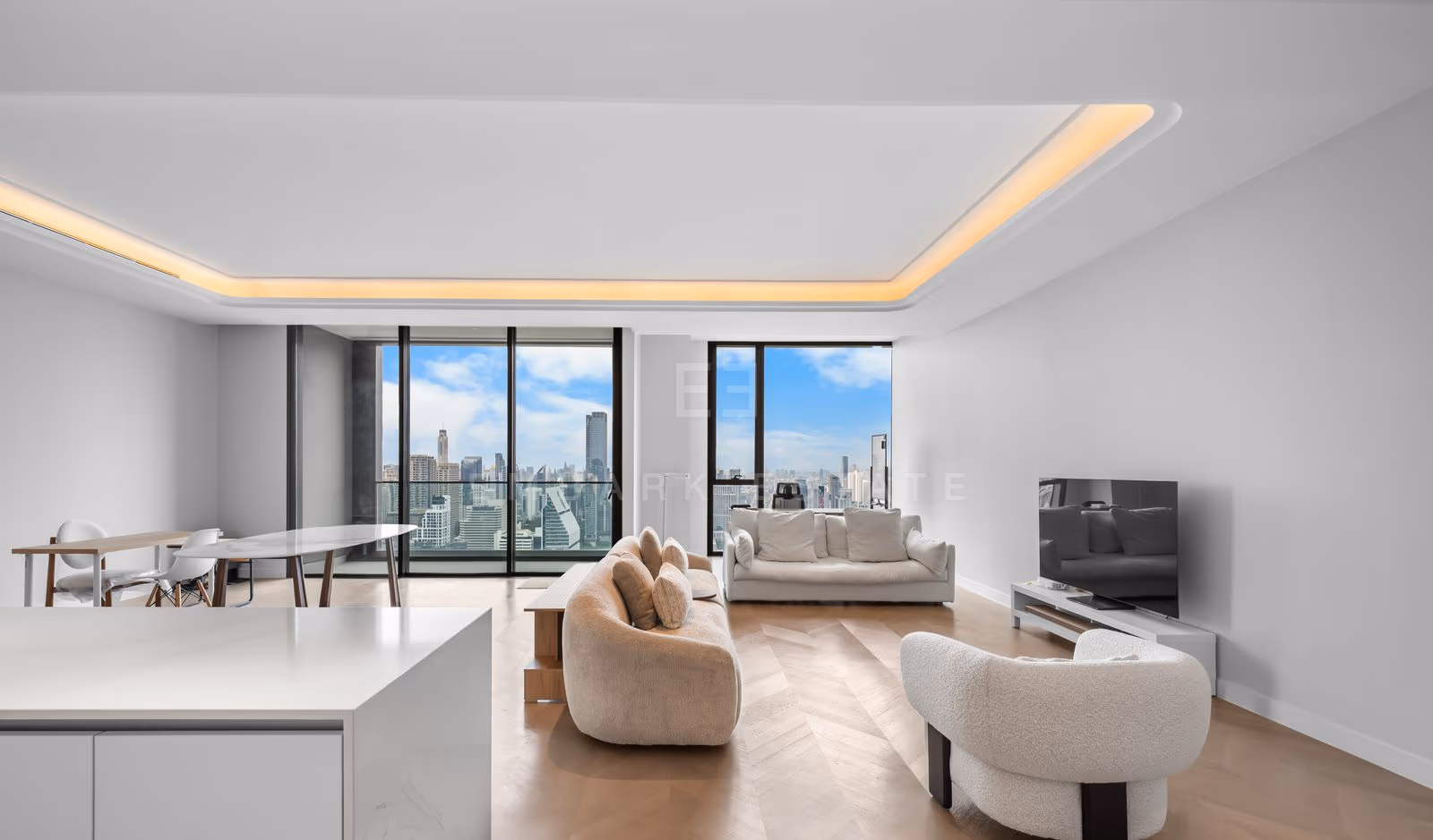 Living room of a three-bedroom residence on the 34th floor of ONE89 Wireless, Bangkok, with two curved cream sofas on herringbone oak floors, a cove-lit ceiling and floor-to-ceiling windows over the city.