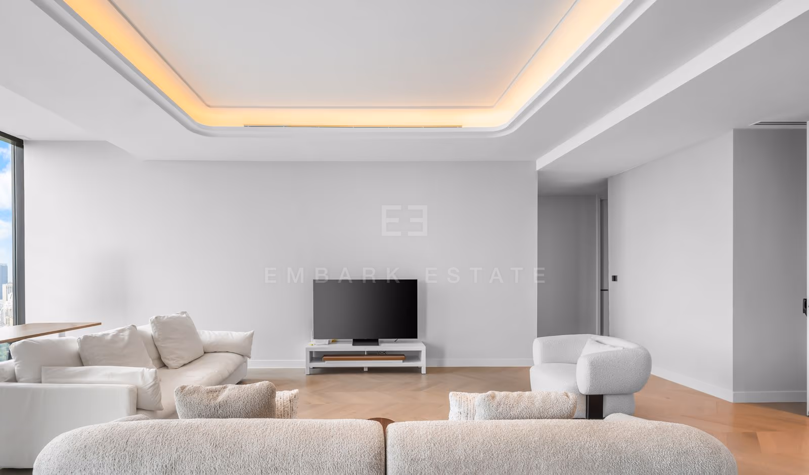 Living room of a three-bedroom residence at ONE89 Wireless, Bangkok, seen across the sofas towards the television wall, with a cove-lit ceiling and herringbone oak floors.