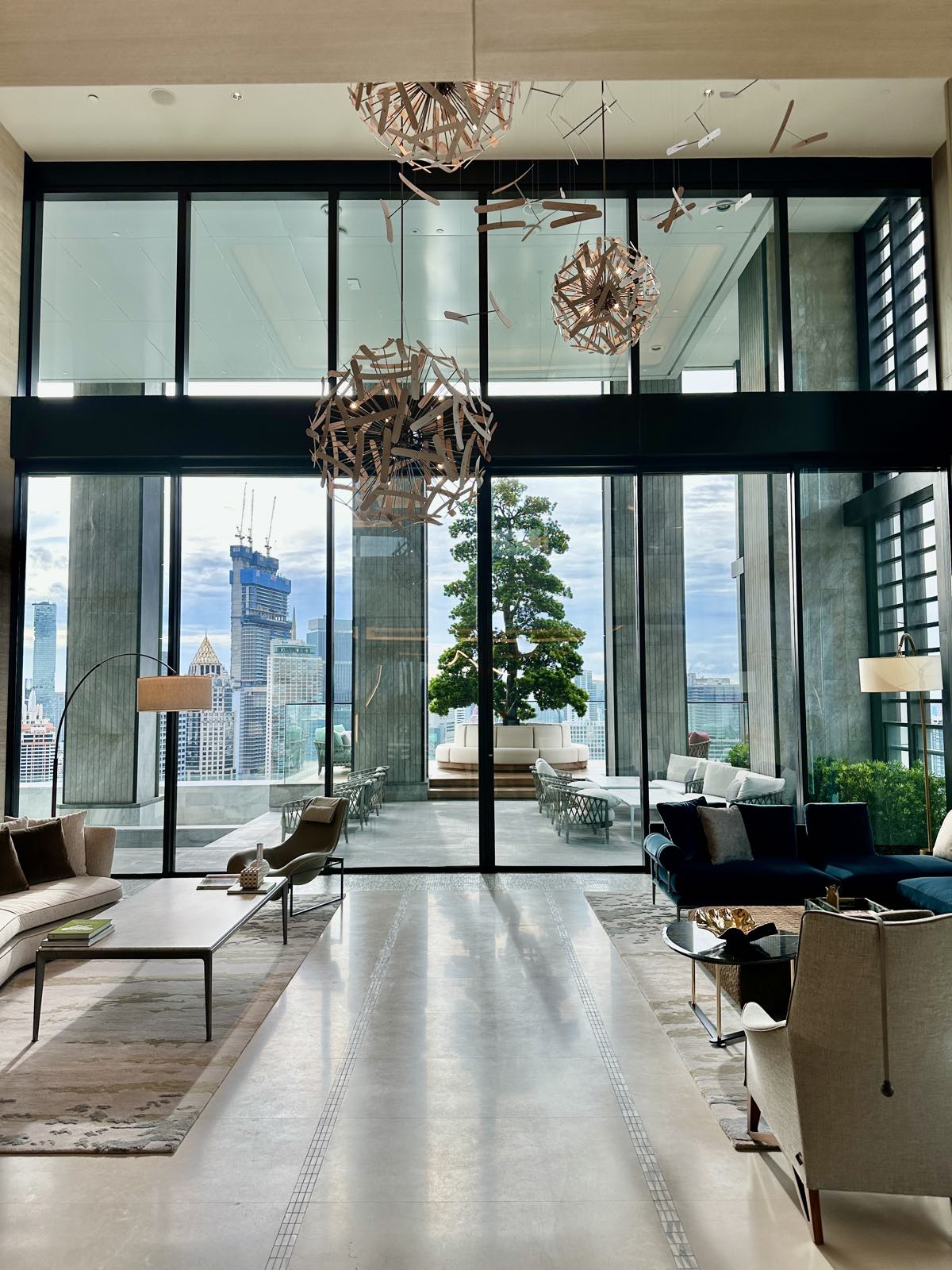 The double-height residents' lounge at ONE89 Wireless, One Bangkok, with sculptural lighting and floor-to-ceiling views over central Bangkok