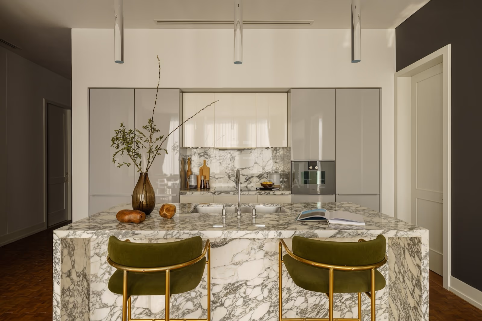 The kitchen of a two-bedroom residence at The Ritz-Carlton Residences Bangkok, with a marble island, integrated appliances and pale lacquered cabinetry