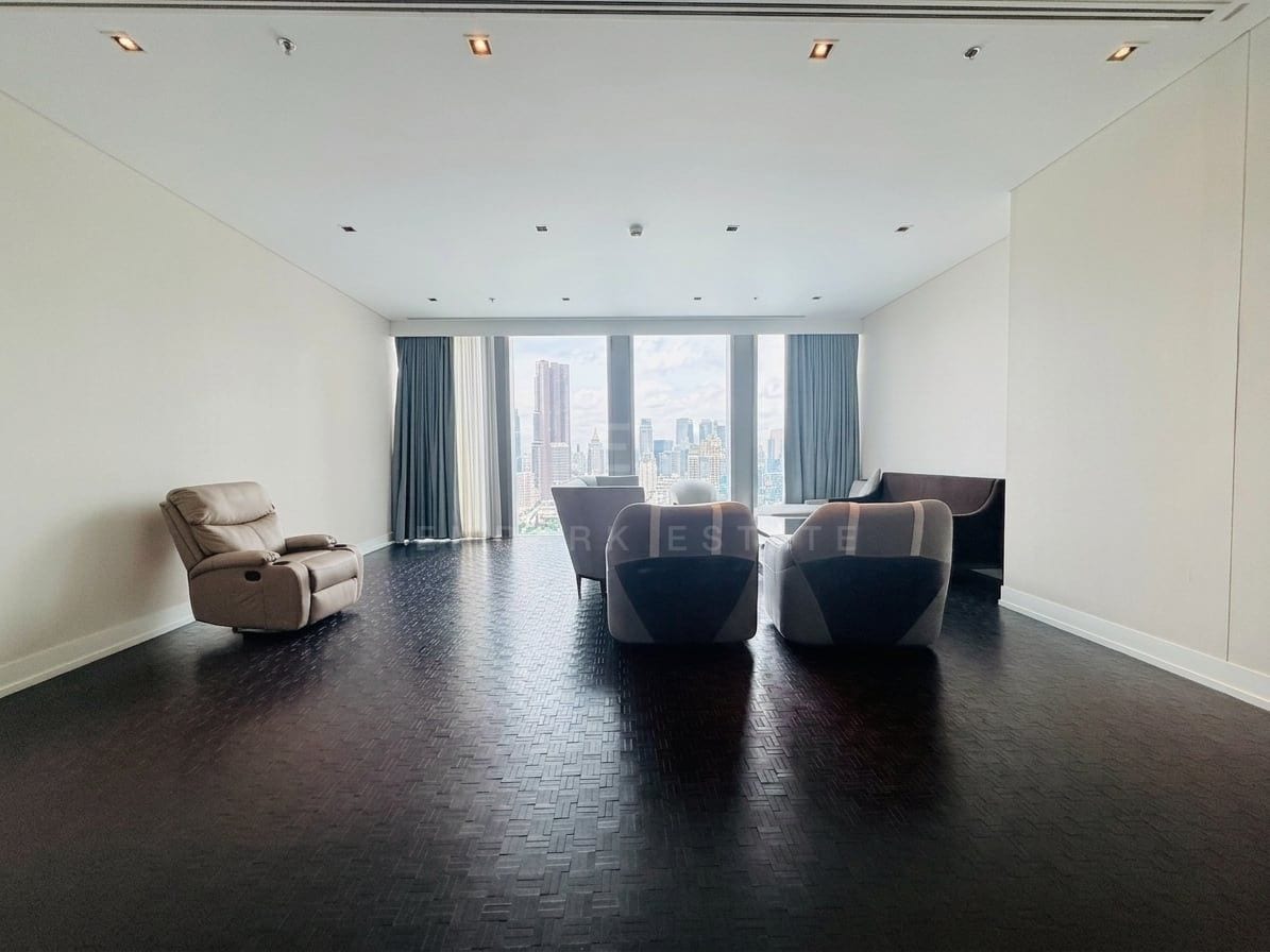 The living room of a three-bedroom residence at The Ritz-Carlton Residences Bangkok, with a few armchairs and a recliner on dark parquet, curtains drawn back from full-height windows over the Bangkok skyline