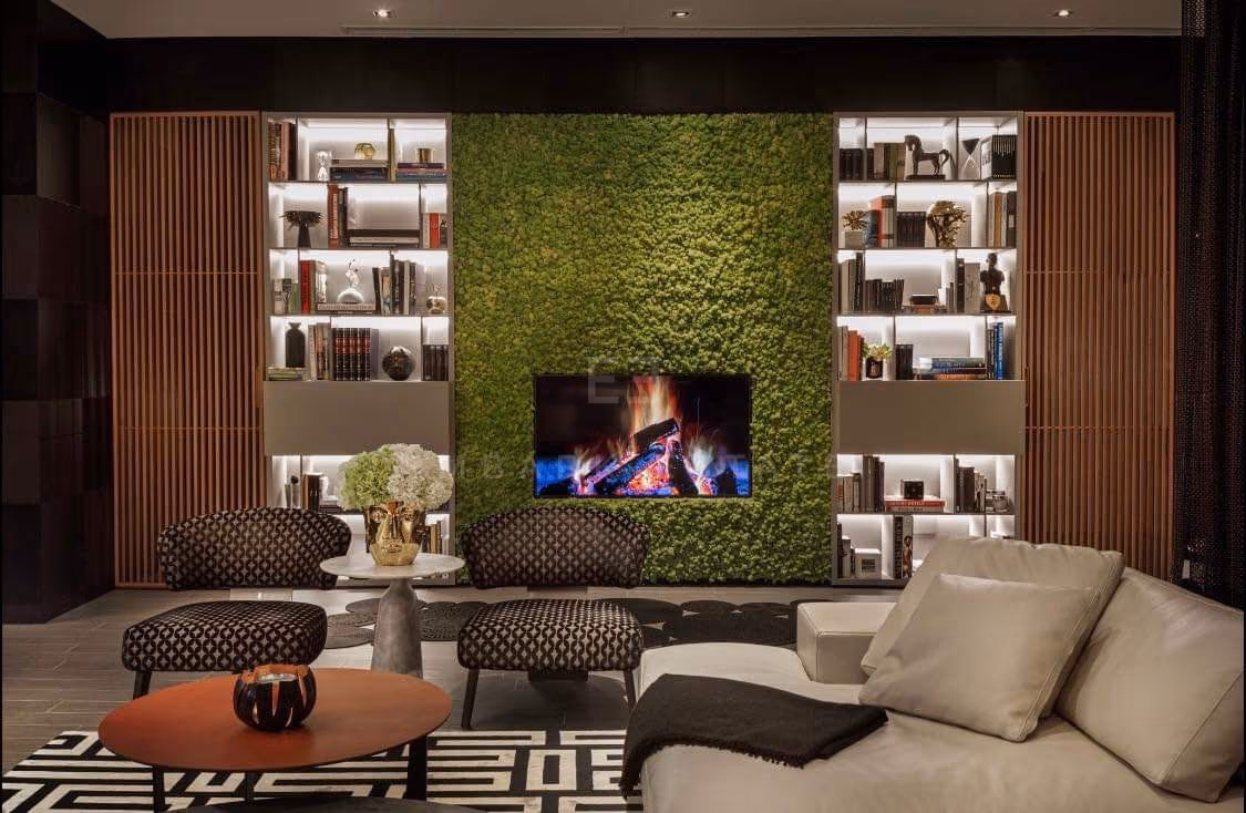 The living room of a two-bedroom residence at The Ritz-Carlton Residences Bangkok, a planted green wall between dark timber shelving, with a fireplace at its centre