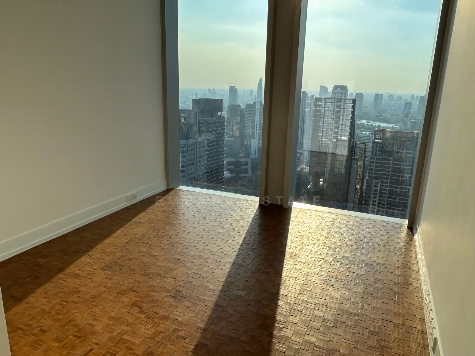 The living room of a two-bedroom residence at The Ritz-Carlton Residences Bangkok, unfurnished, with sunlight falling across the floor and the skyline through the corner glazing