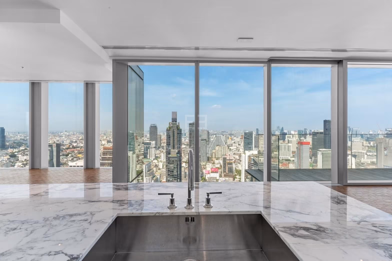 The kitchen counter of a two-bedroom residence at The Ritz-Carlton Residences Bangkok, veined marble with an integrated sink against full-height city glass