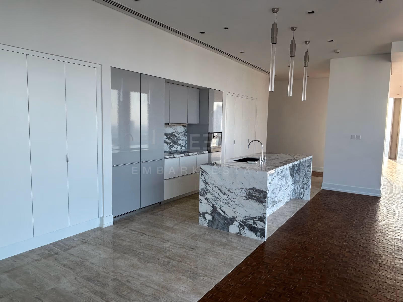 The kitchen of a two-bedroom residence at The Ritz-Carlton Residences Bangkok, a veined marble island under slim pendants beside full-height windows