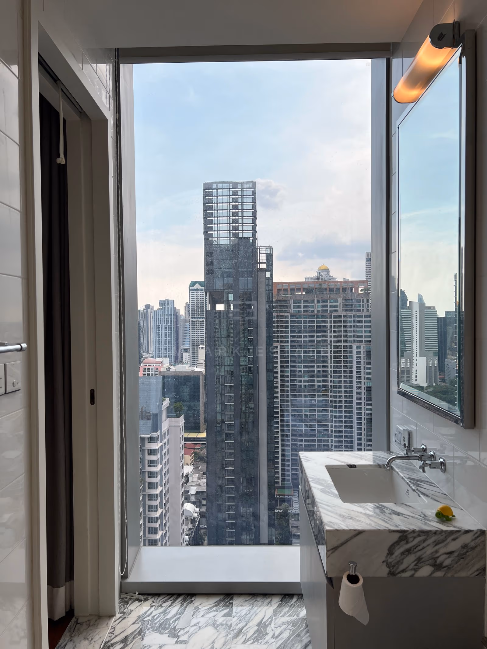 The guest cloakroom on the 31st floor at The Ritz-Carlton Residences Bangkok, a marble vanity beneath a mirror beside a window over the city