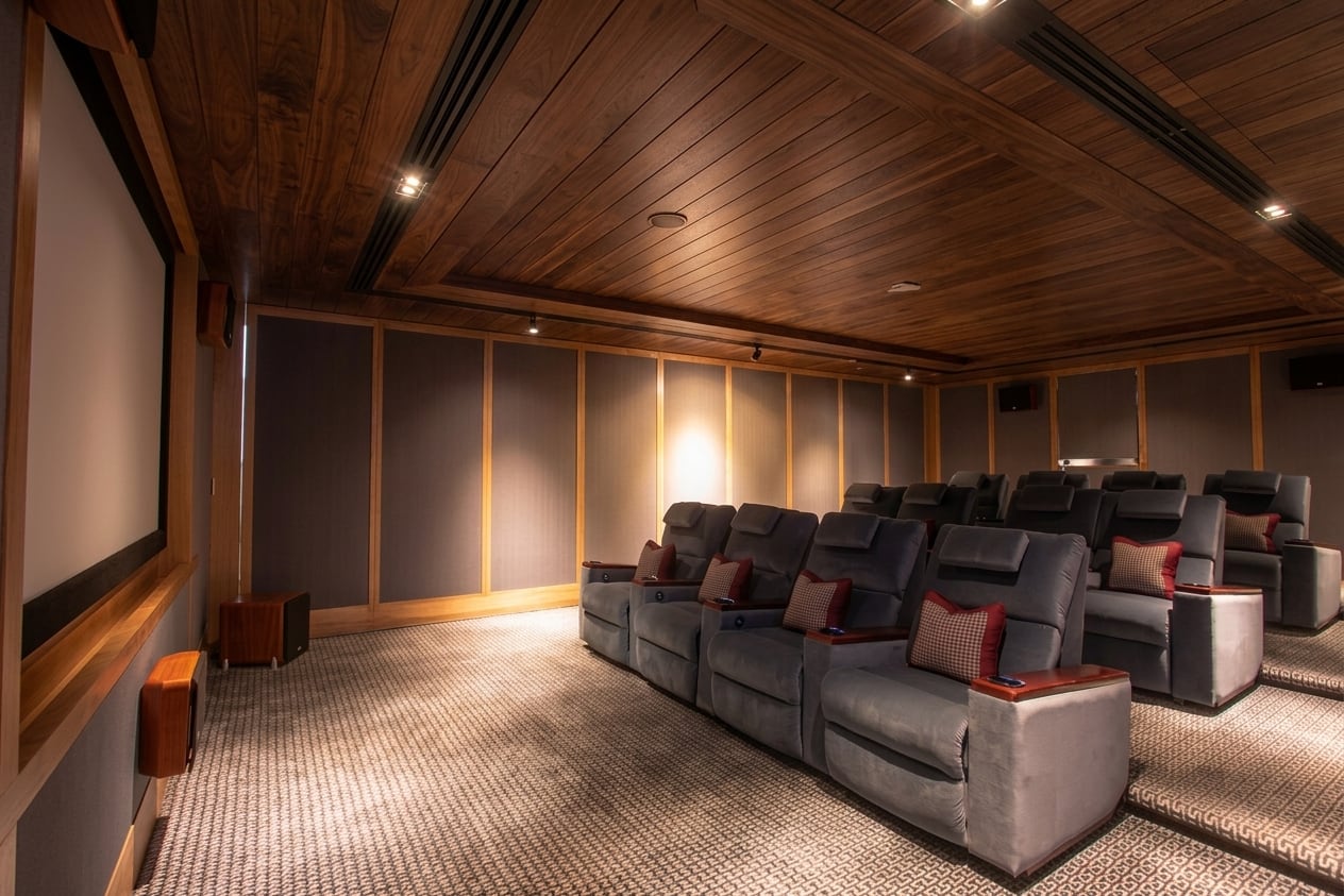 The private cinema at The Ritz-Carlton Residences Bangkok: tiered rows of grey reclining seats facing a projection screen, in a room panelled and ceilinged in walnut