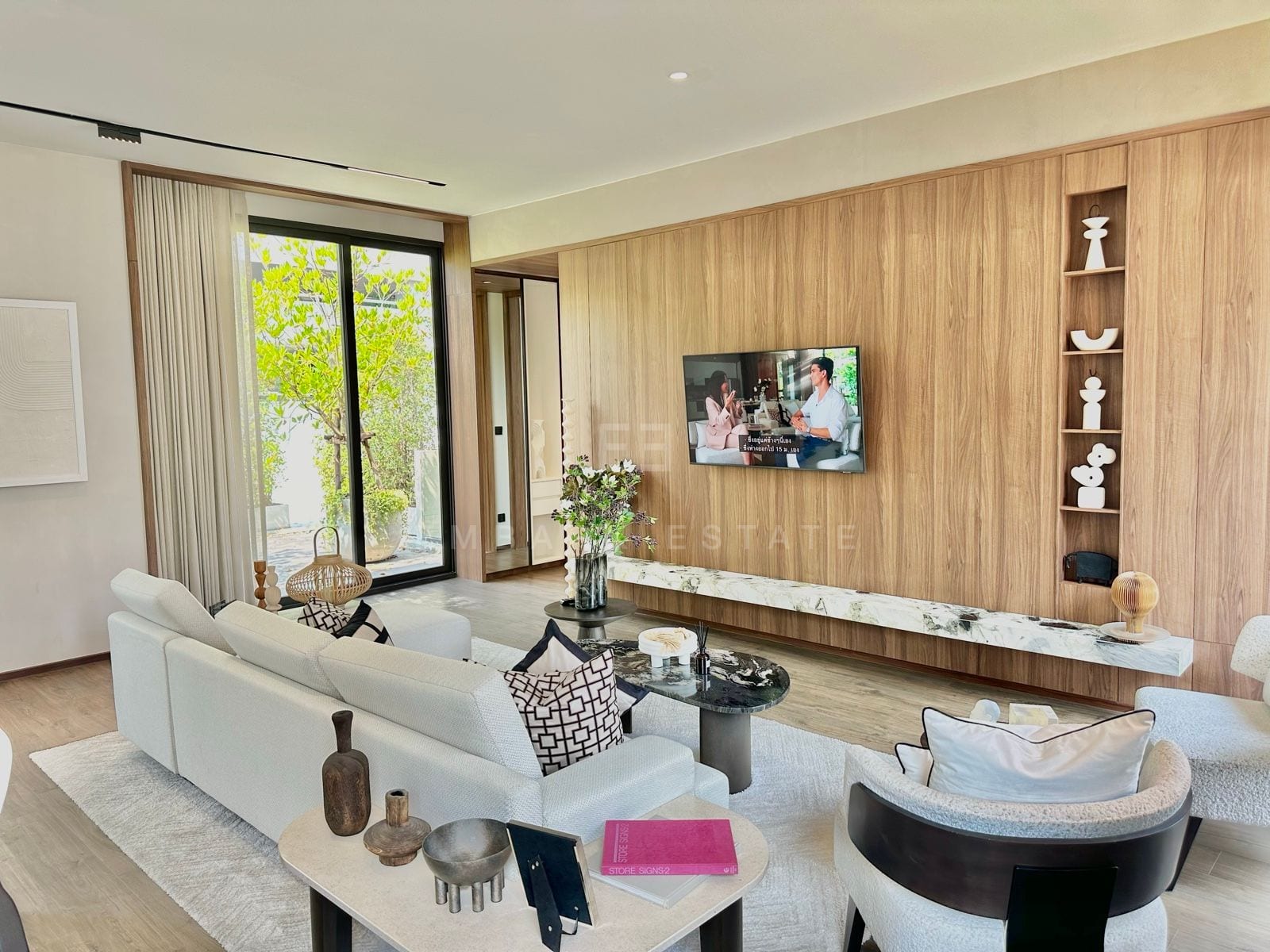 Living area with a white sectional sofa, marble-topped coffee tables, wall-mounted television on a timber feature wall and a floating stone console beside floor-to-ceiling glazing, a 2-bedroom villa at ROMM Convent, Bangkok