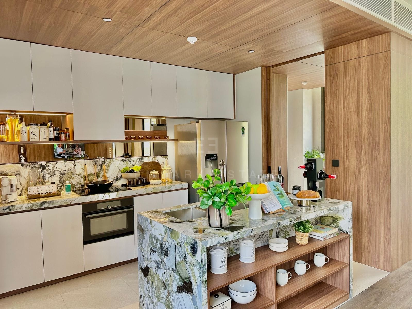 Open kitchen with a marble waterfall island, full-height white cabinetry, stainless steel refrigerator, built-in oven and a timber ceiling, a 2-bedroom villa at ROMM Convent, Bangkok