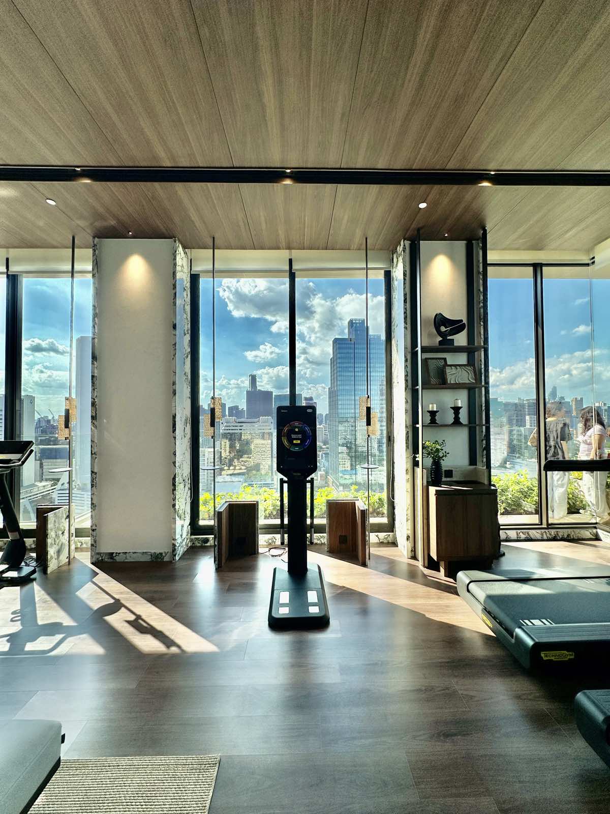 Fitness room with a smart-mirror trainer and floor-to-ceiling glazing at ROMM Convent, Bangkok.
