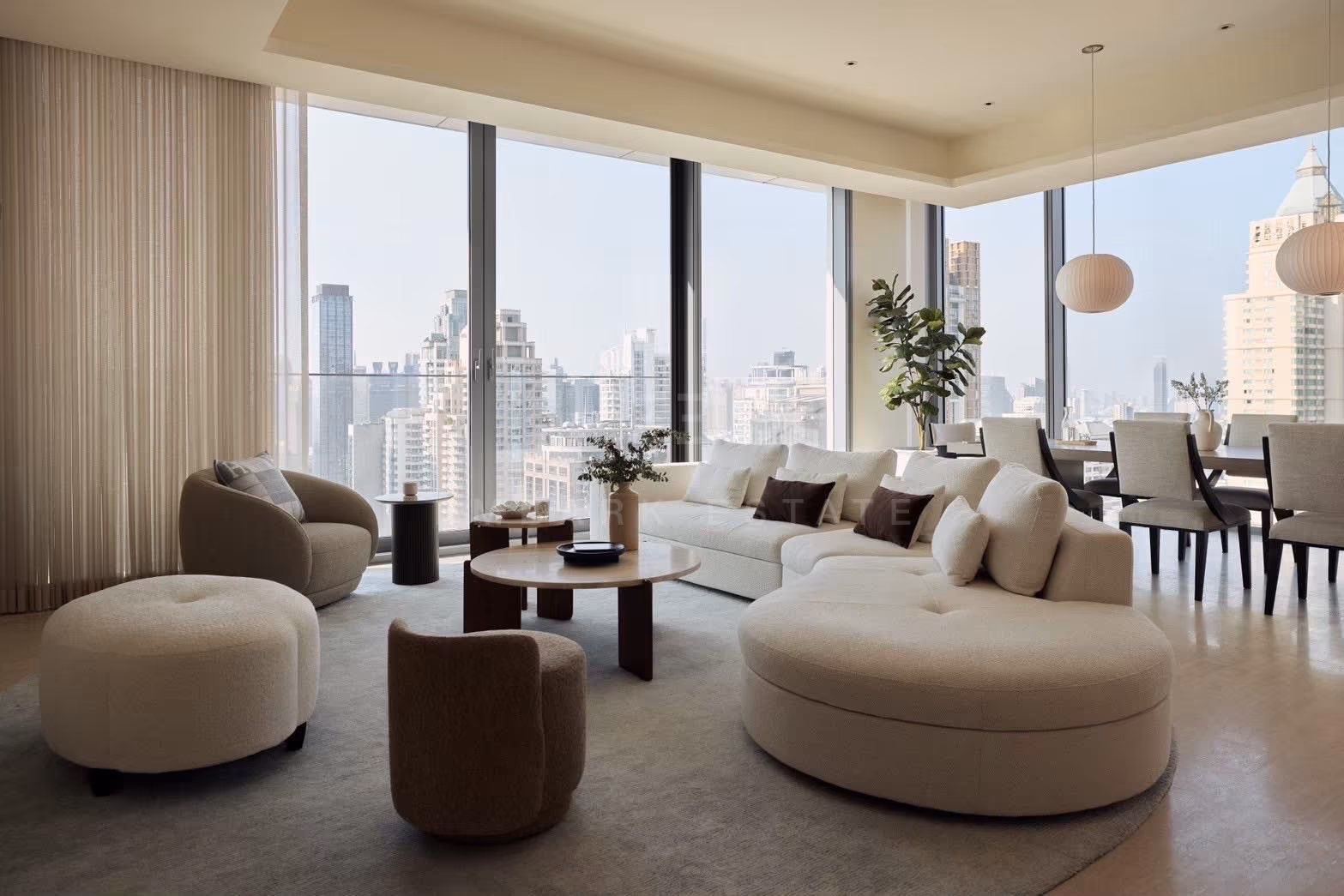The corner living and dining room of a 3-bedroom residence at Scope Langsuan, Bangkok, with a curved cream sofa, a travertine coffee table, a dining table for eight and floor-to-ceiling glass on two sides over the city skyline