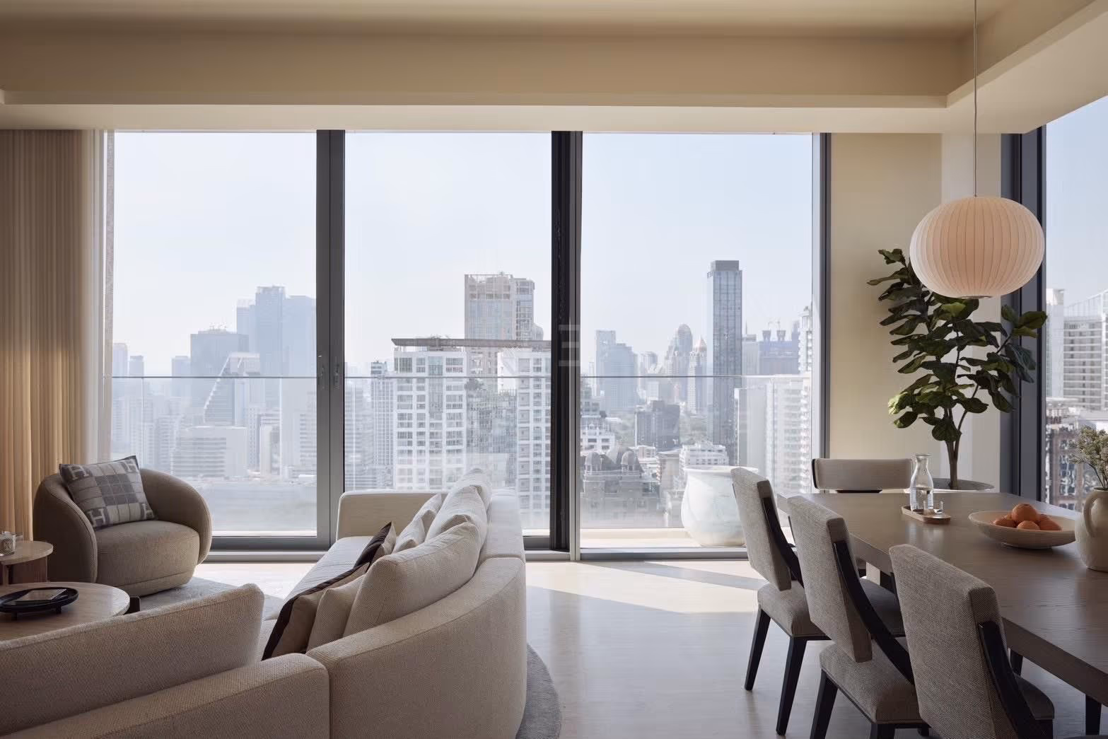 The living and dining room of a 3-bedroom residence at Scope Langsuan, Bangkok, with a paper pendant lamp over the dining table and floor-to-ceiling windows framing the central Bangkok skyline