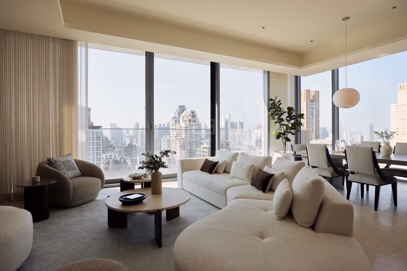 The living room of a 3-bedroom residence at Scope Langsuan, Bangkok, with a curved sectional sofa and a corner of floor-to-ceiling glass looking over the towers of central Bangkok