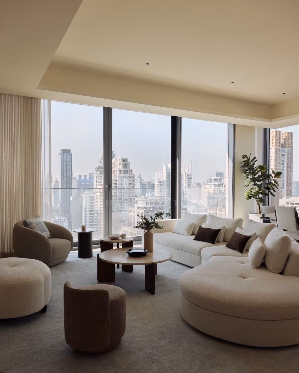 The lounge of a 3-bedroom residence at Scope Langsuan, Bangkok, with bouclé armchairs, a curved cream sofa and sheer curtains drawn back from floor-to-ceiling windows
