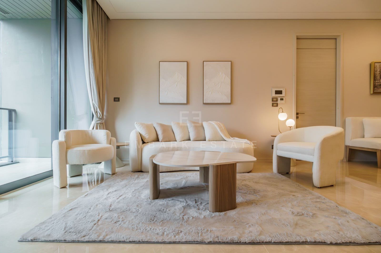 The living room of the two-bedroom residence at the Residences at Sindhorn Kempinski, Bangkok, with a cream sofa, two armchairs and floor-to-ceiling windows