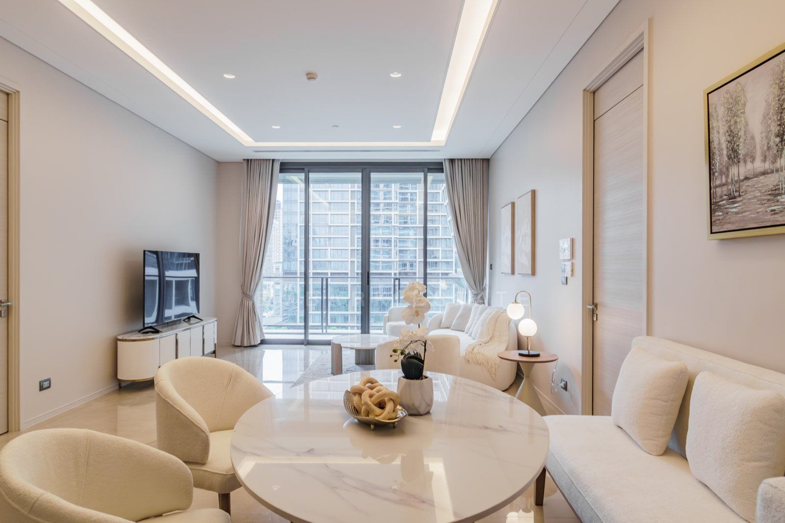 The living room of the two-bedroom residence at the Residences at Sindhorn Kempinski, Bangkok, with cream sofas and a window over the central Bangkok skyline