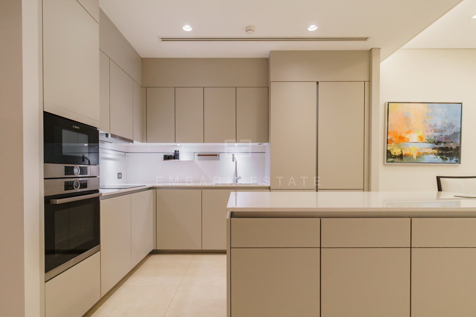 The kitchen of the two-bedroom residence at the Residences at Sindhorn Kempinski, Bangkok, with beige cabinetry, Bosch ovens, a stone island and abstract art