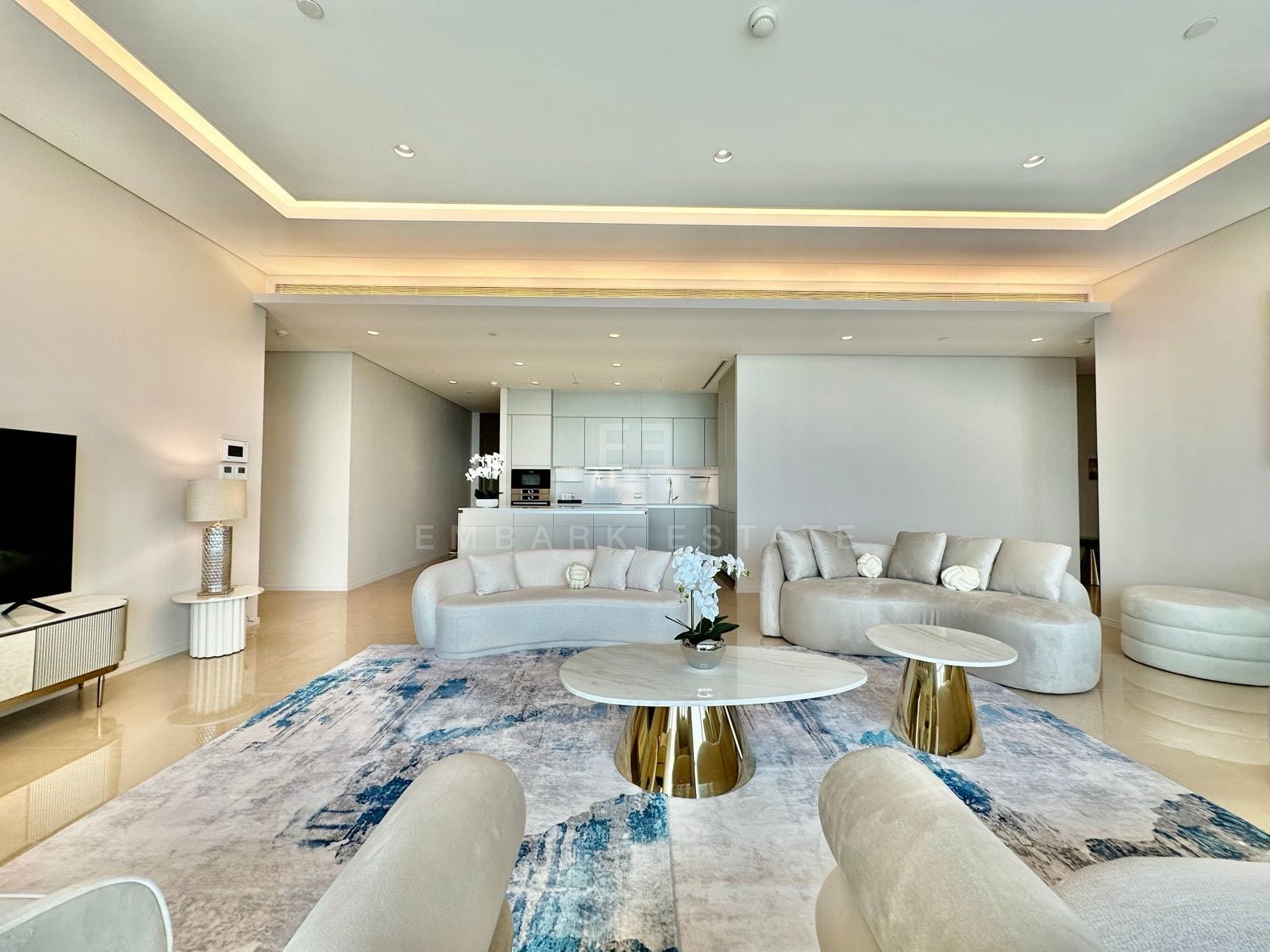 The open living room of the 5-bedroom residence at the Residences at Sindhorn Kempinski, Bangkok, with curved cream sofas and an open kitchen behind